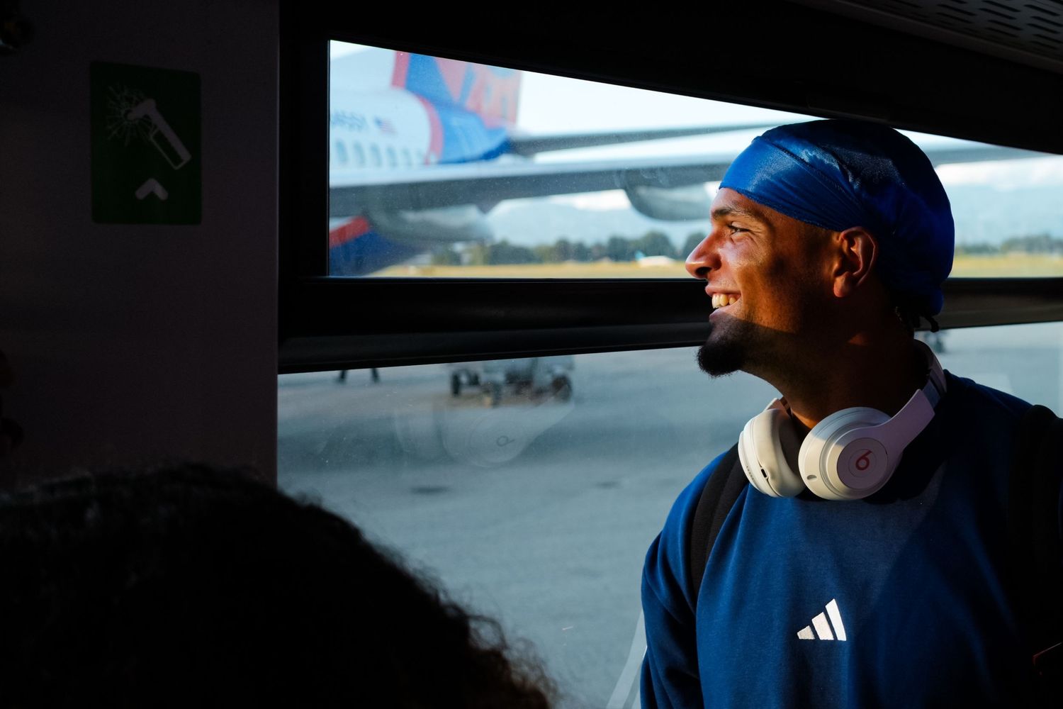 Passenger wearing headphones looks out a vehicle window toward an airplane on the tarmac.