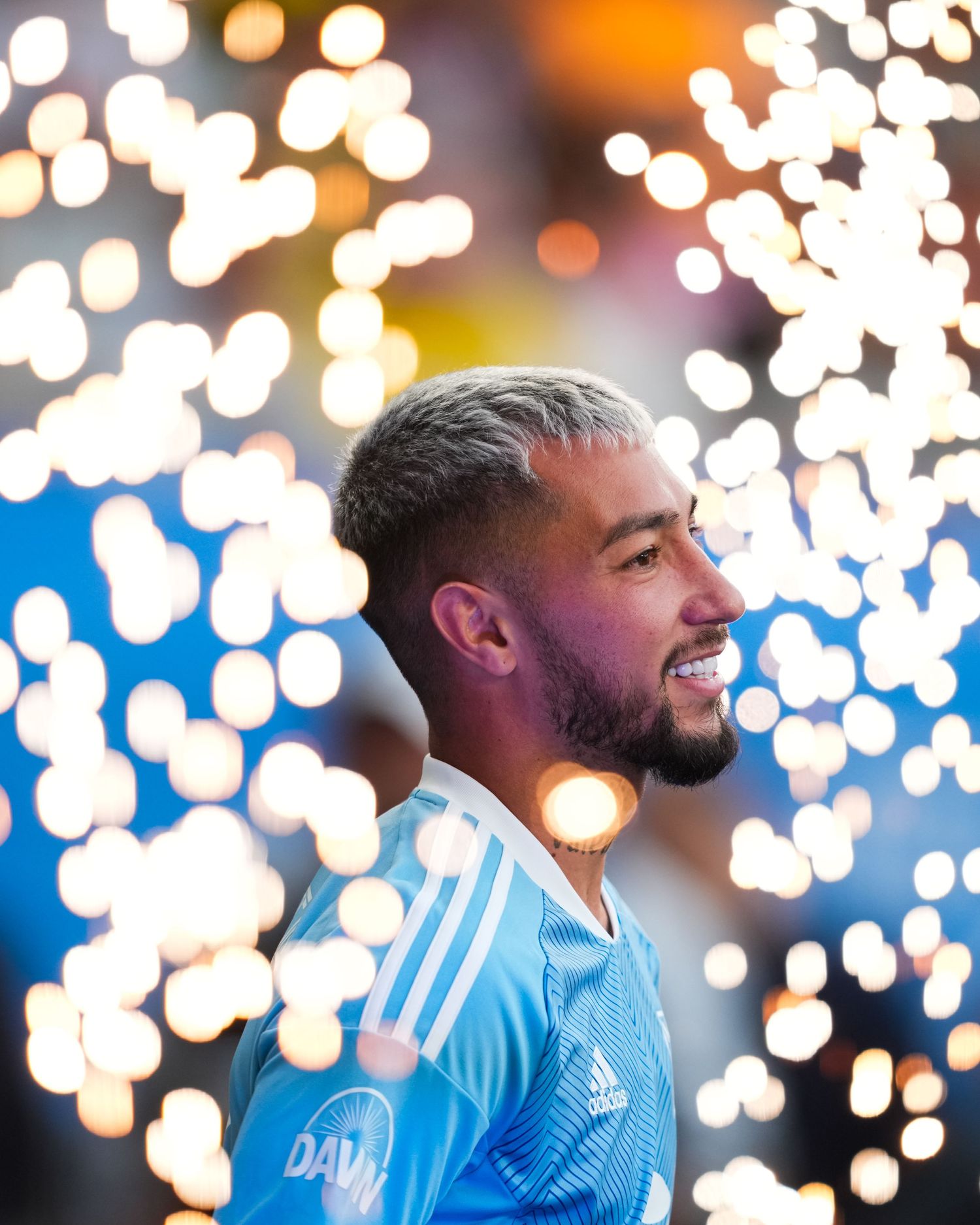 Soccer player poses during an event while surrounded by bright sparkling lights in the background.