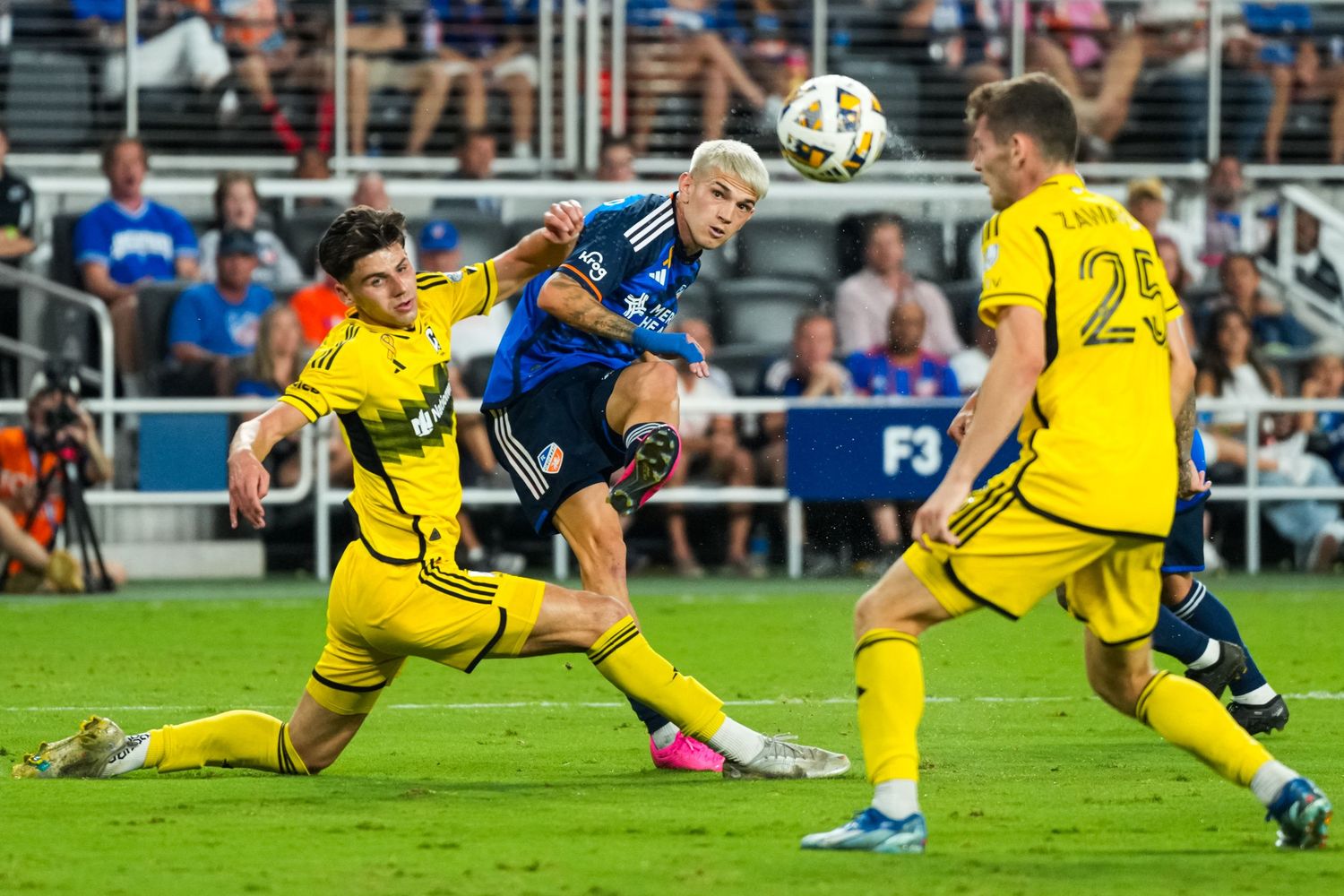 FC Cincinnati player strikes the ball while defenders attempt to block the shot during a match.