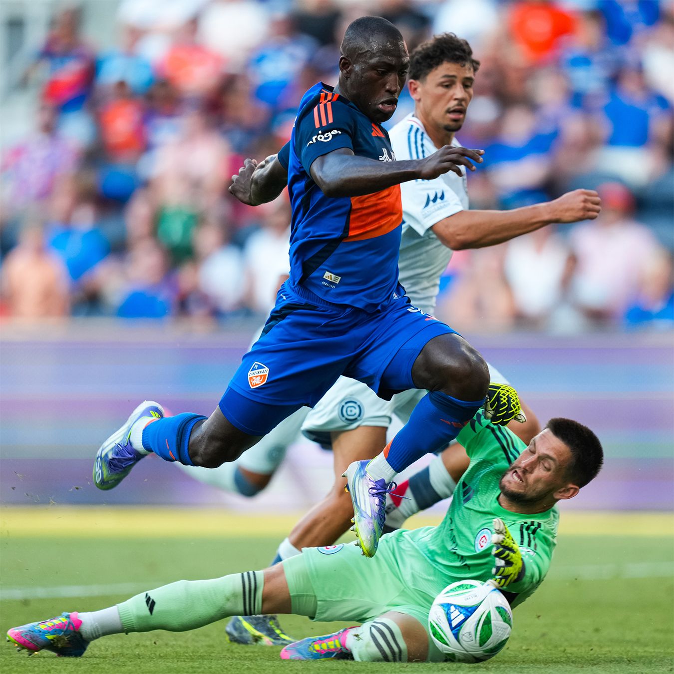 FC Cincinnati player leaps over a goalkeeper making a challenge during a soccer match.