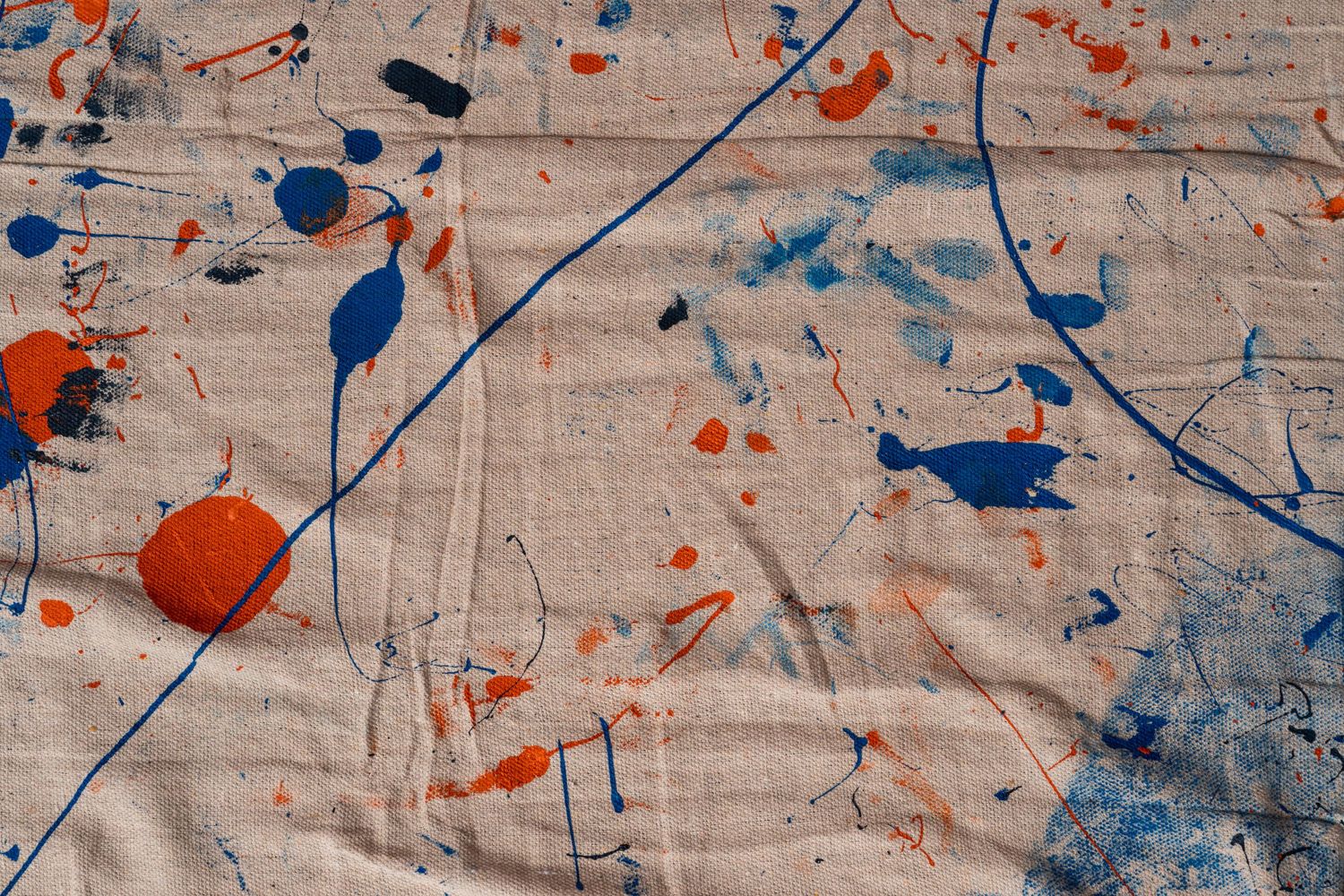 Paint-splattered canvas drop cloth featuring abstract blue, orange, and black paint marks and brushstroke patterns.