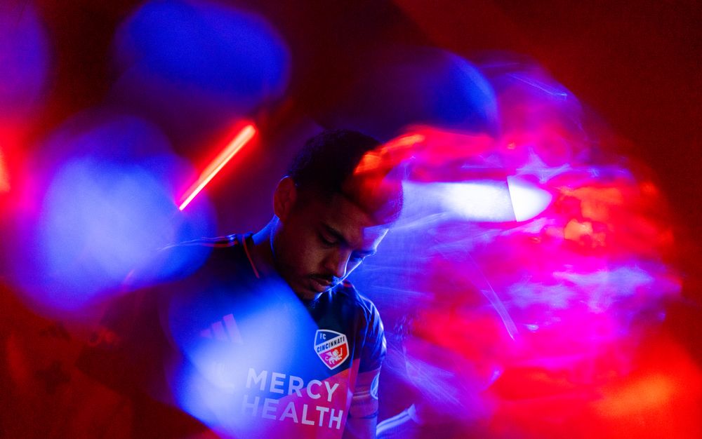 Studio-style portrait of a soccer player surrounded by colorful blue and red lighting effects.