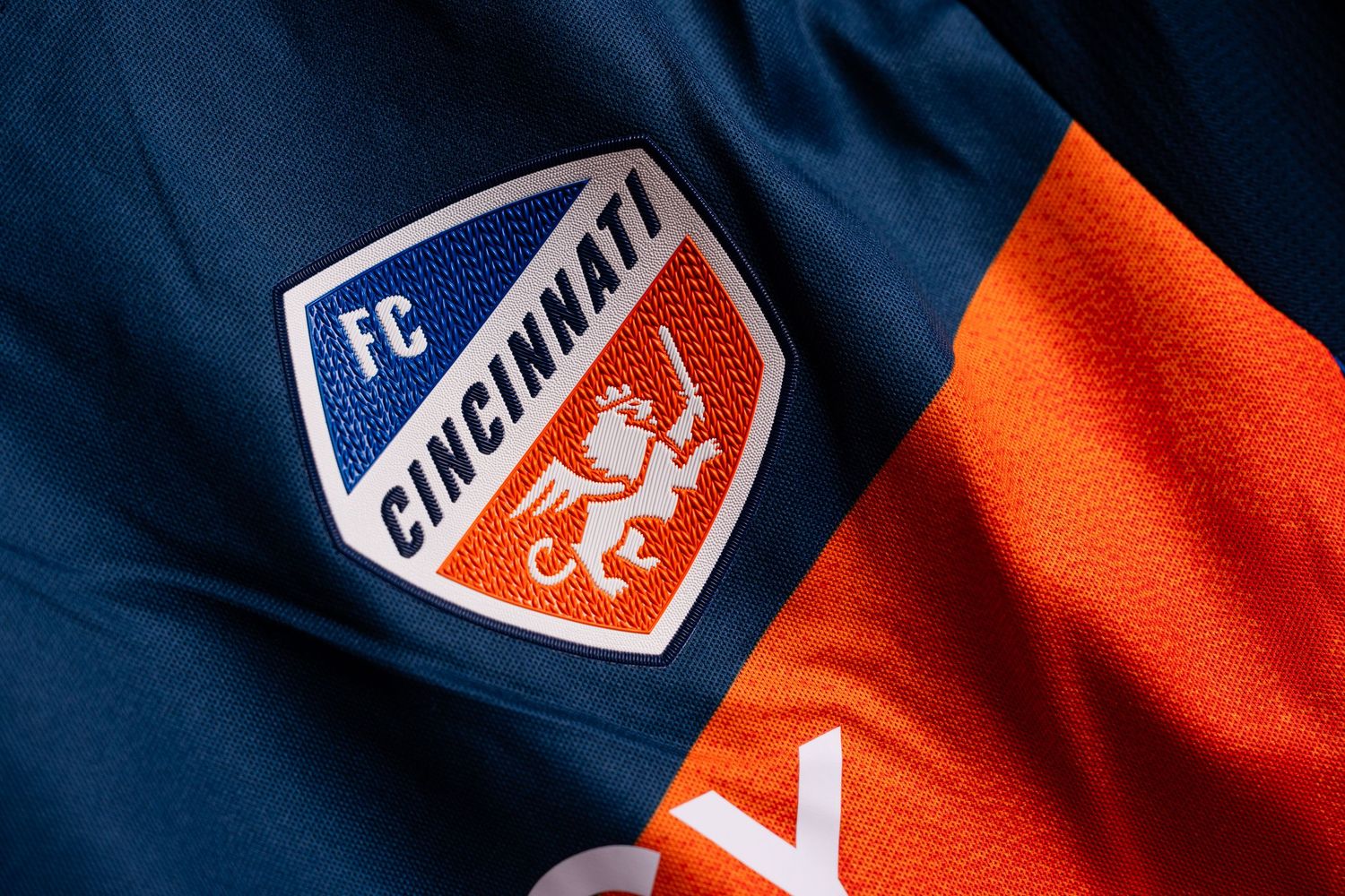 Close-up of the FC Cincinnati crest embroidered on a blue and orange soccer jersey.