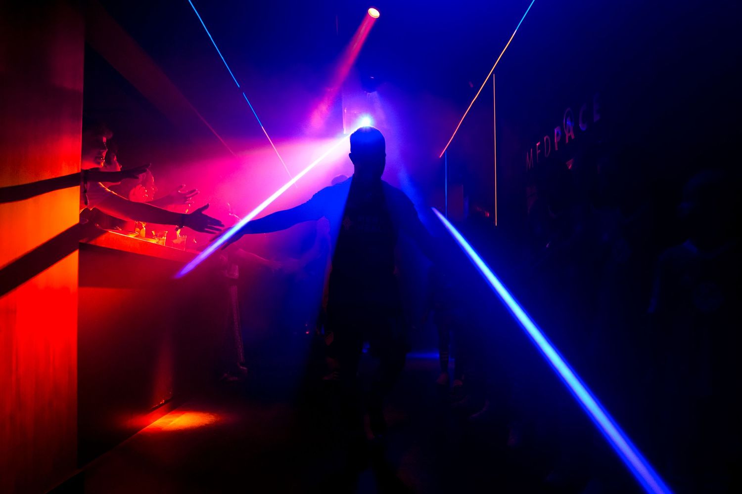 Silhouetted soccer player walks through a tunnel illuminated by blue and red lights before a match.