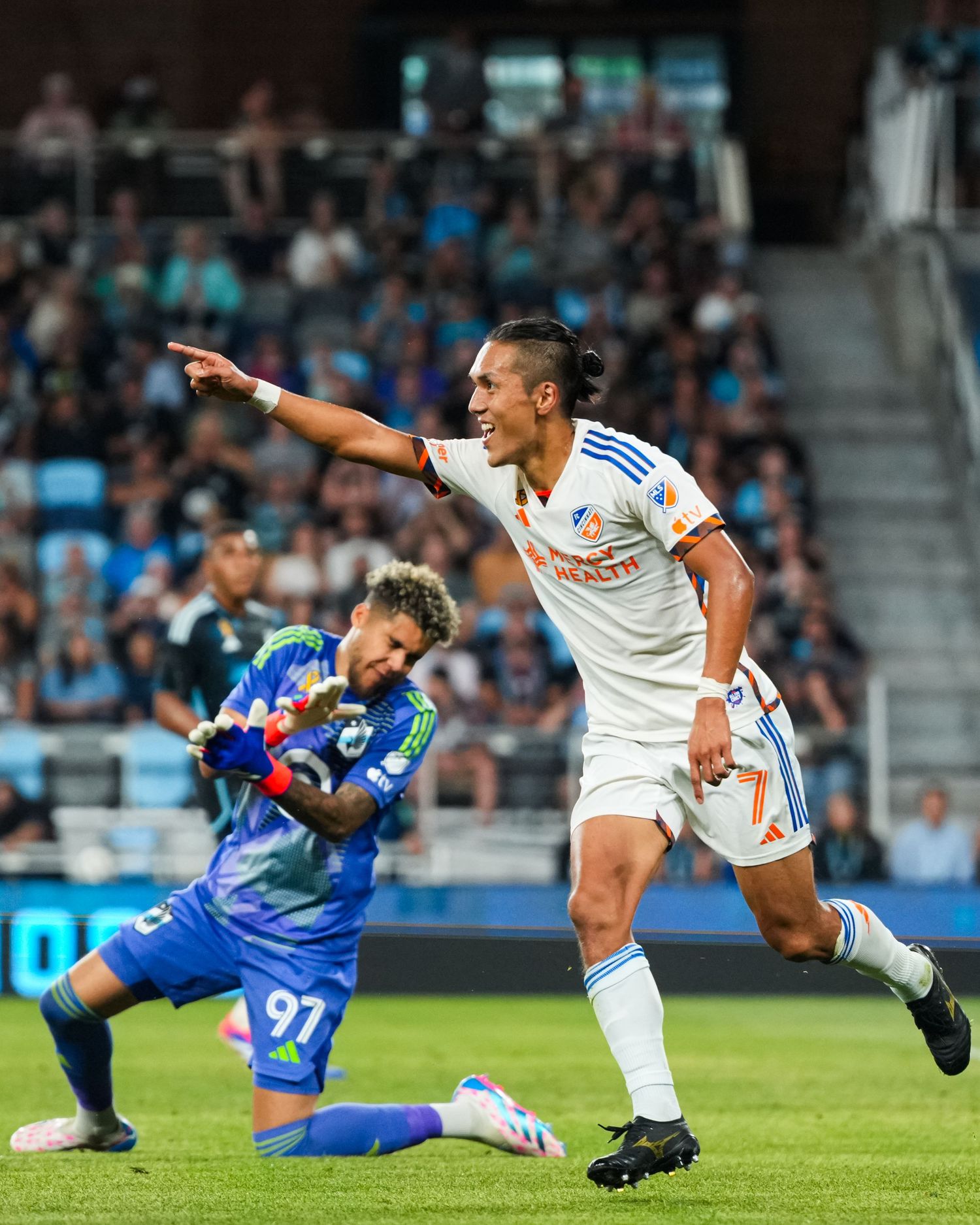 FC Cincinnati player in a white uniform points while running past a goalkeeper during a match.