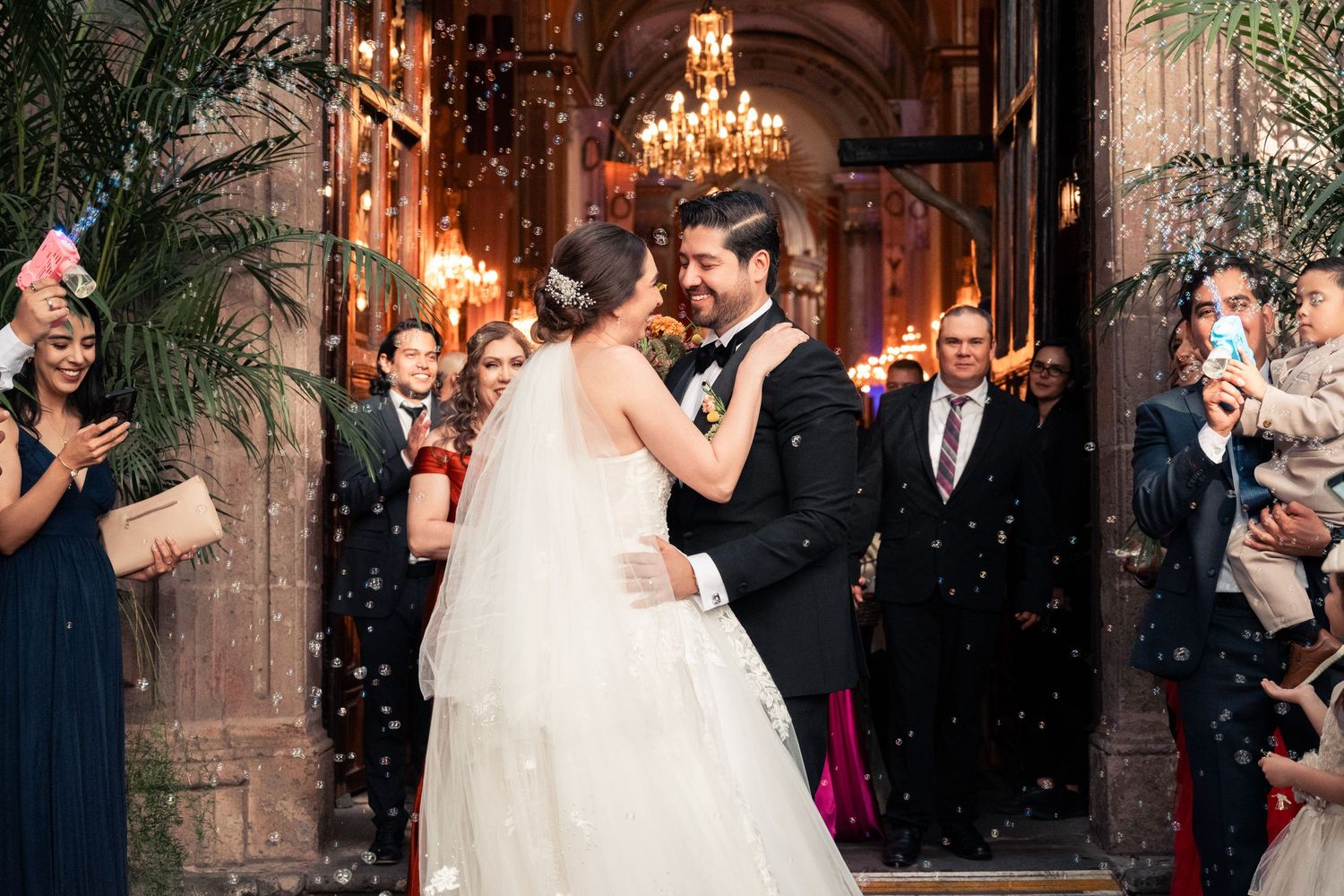 Bride and groom share first dance amid confetti shower at elegant chandelier-lit wedding venue.