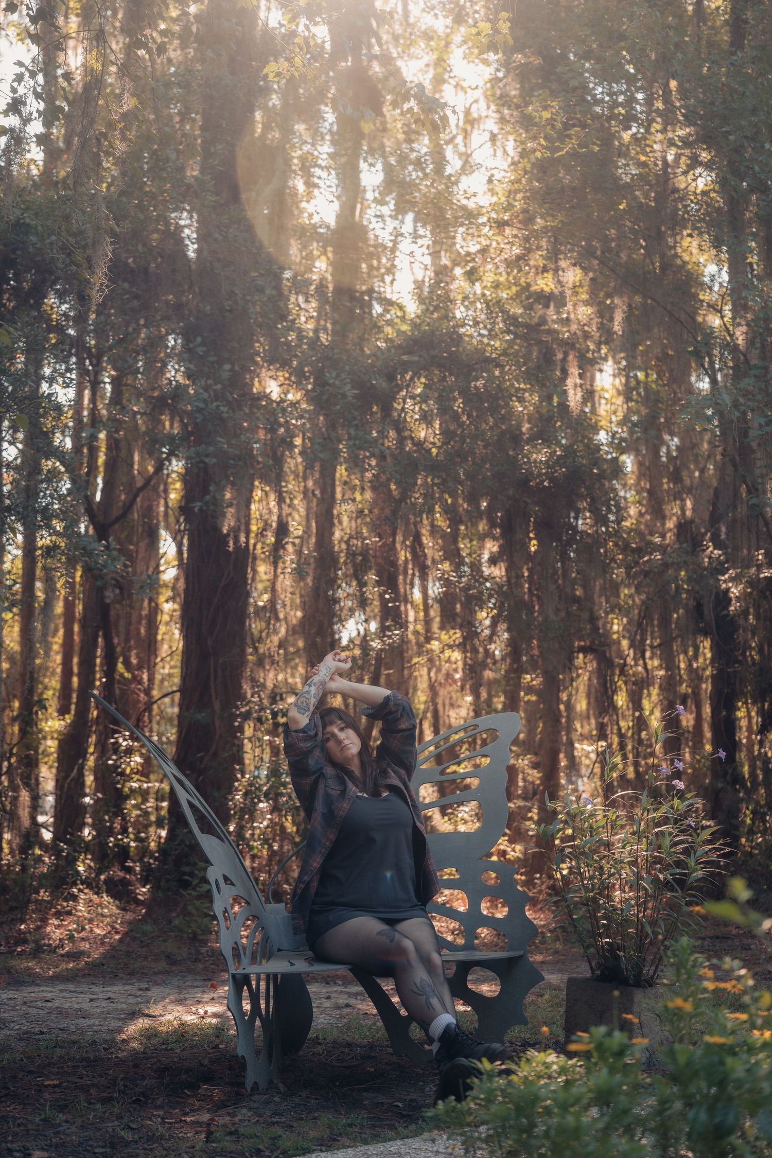 Woman sitting on a decorative bench in a sunlit forest, surrounded by tall trees with golden light filtering through.
