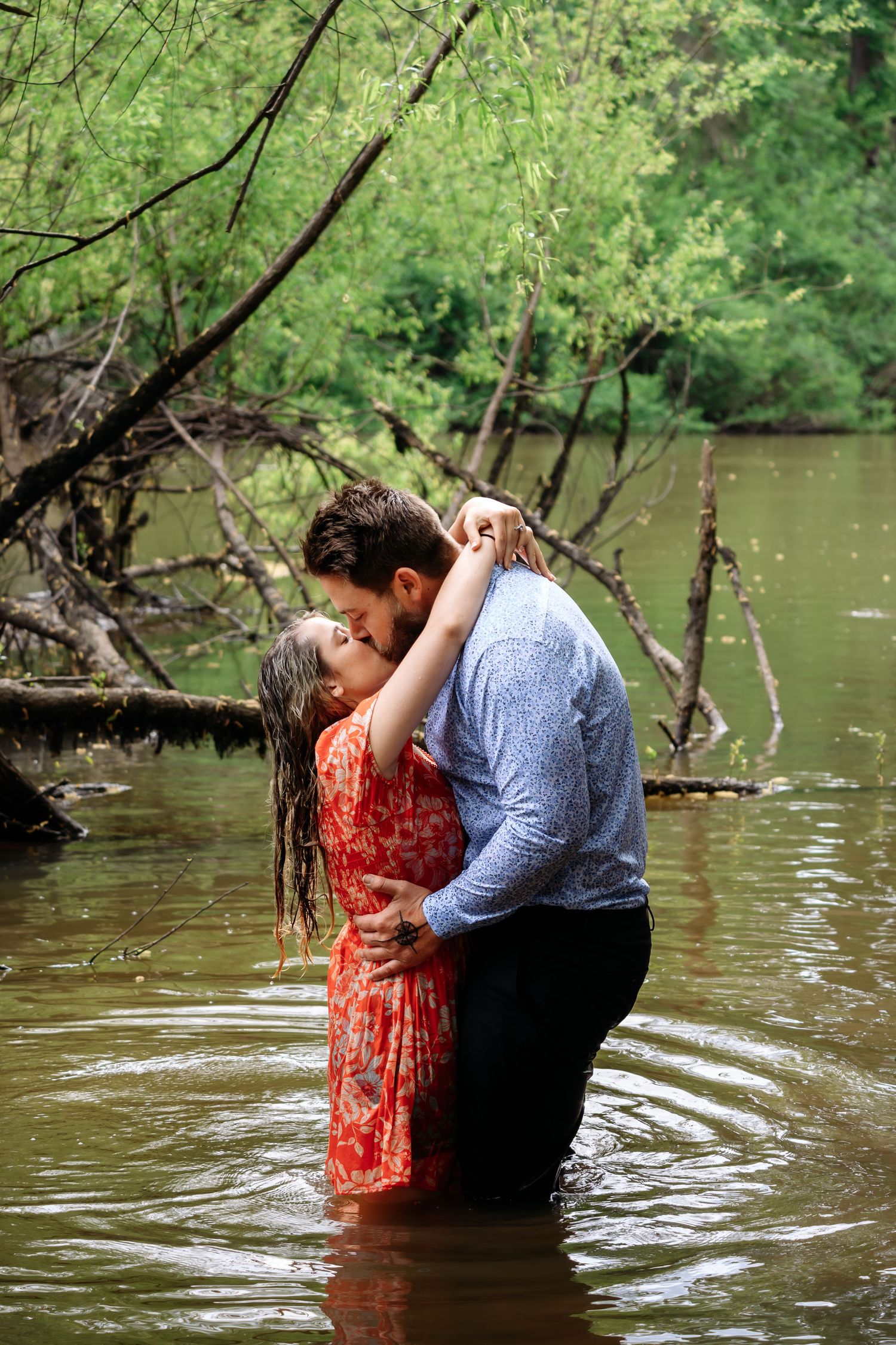 Newly engaged couple kissing passionately while standing waist-deep in a scenic river.