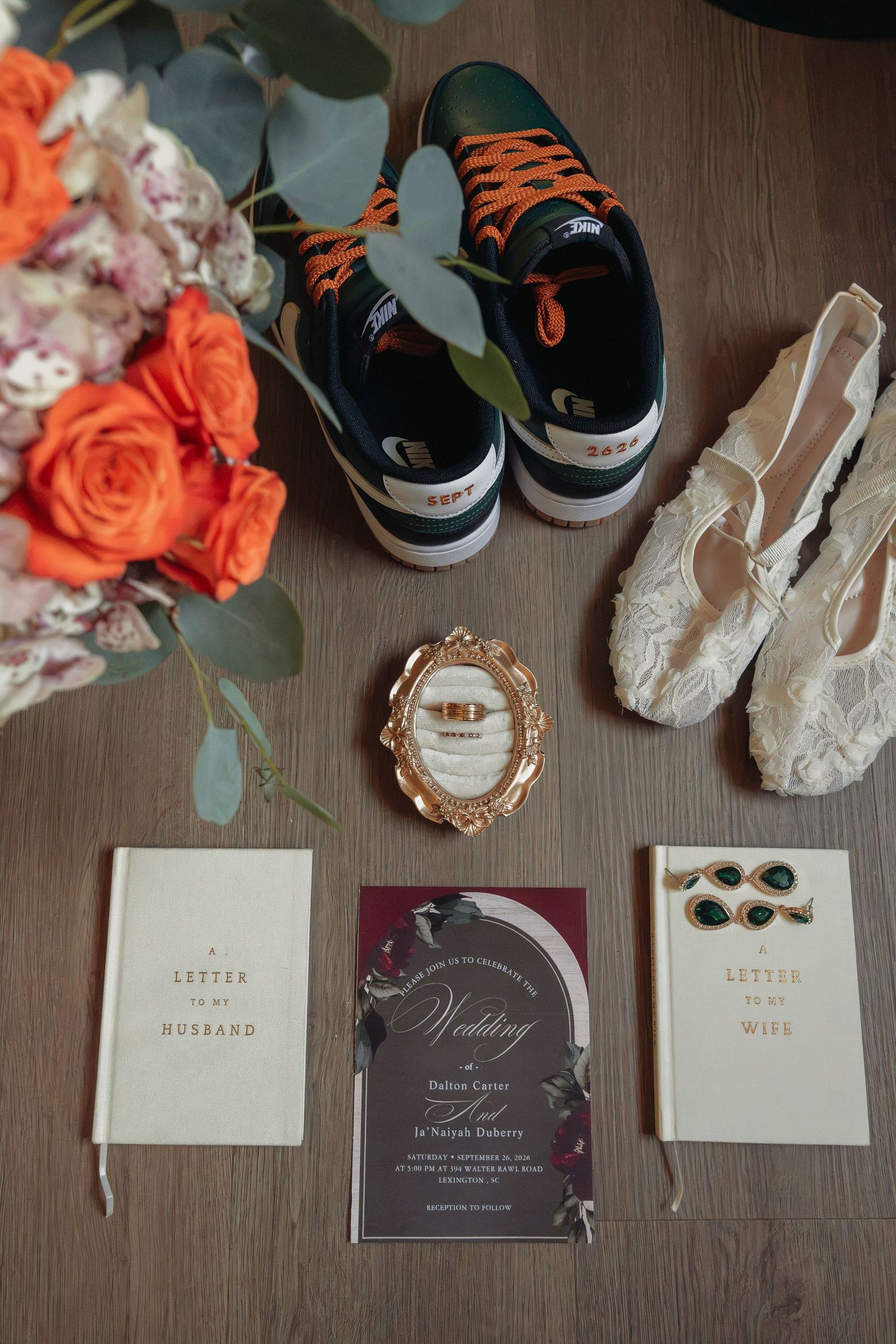Wedding flat lay with sneakers, bridal shoes, bouquet, invitation, and vow books on wooden floor.
