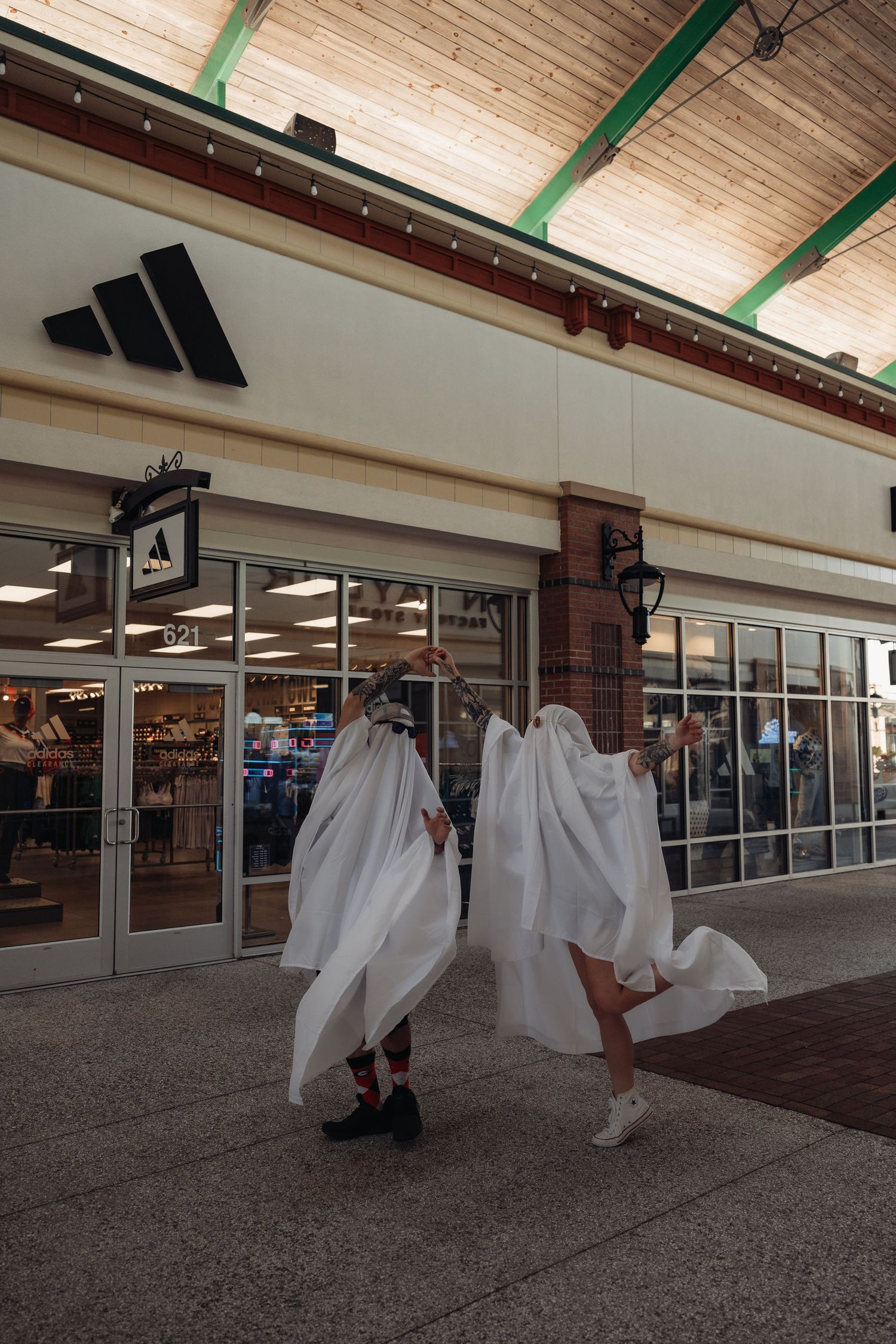 Two people in white ghost costumes dance and wave their sheets outside an Adidas outlet store.