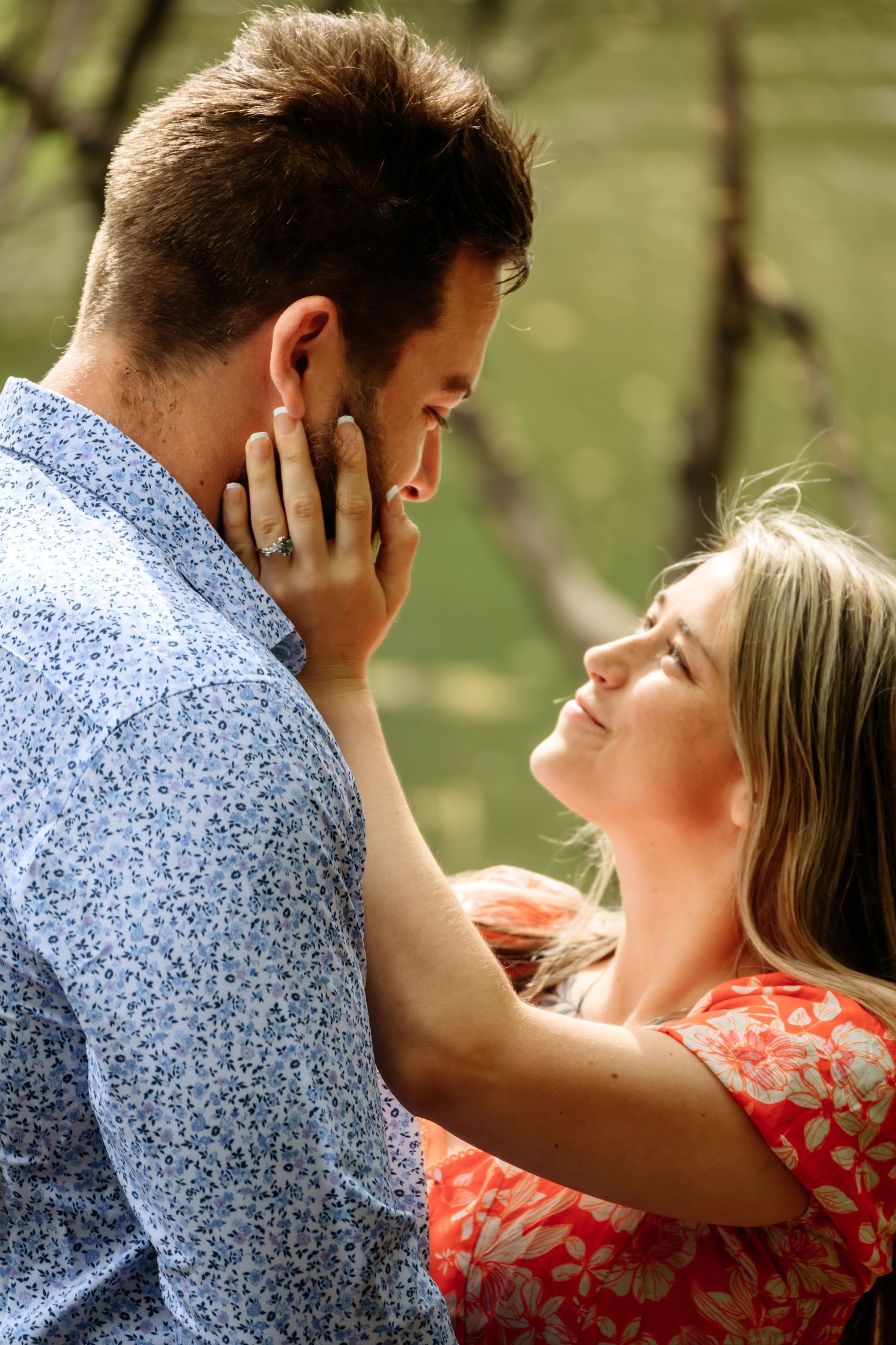Couple sharing a tender moment outdoors, woman touching mans face wearing an engagement ring.