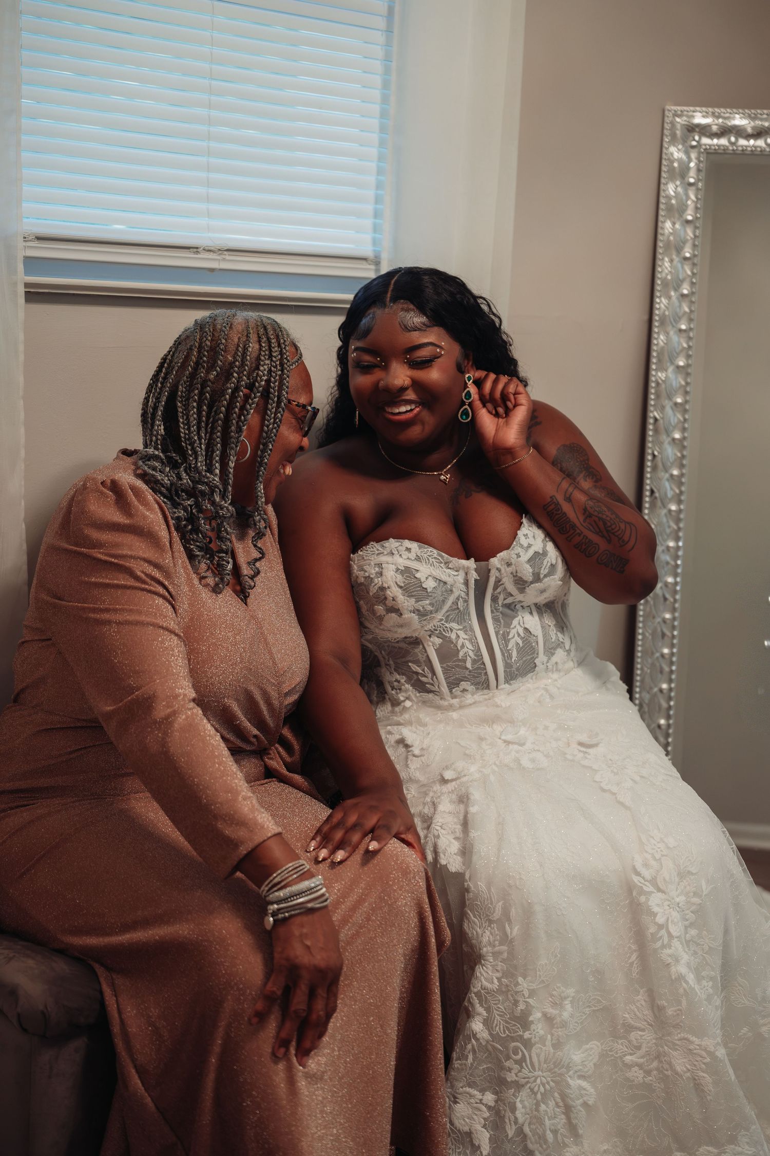 Smiling Black bride in strapless lace gown sharing a joyful moment with her mother.