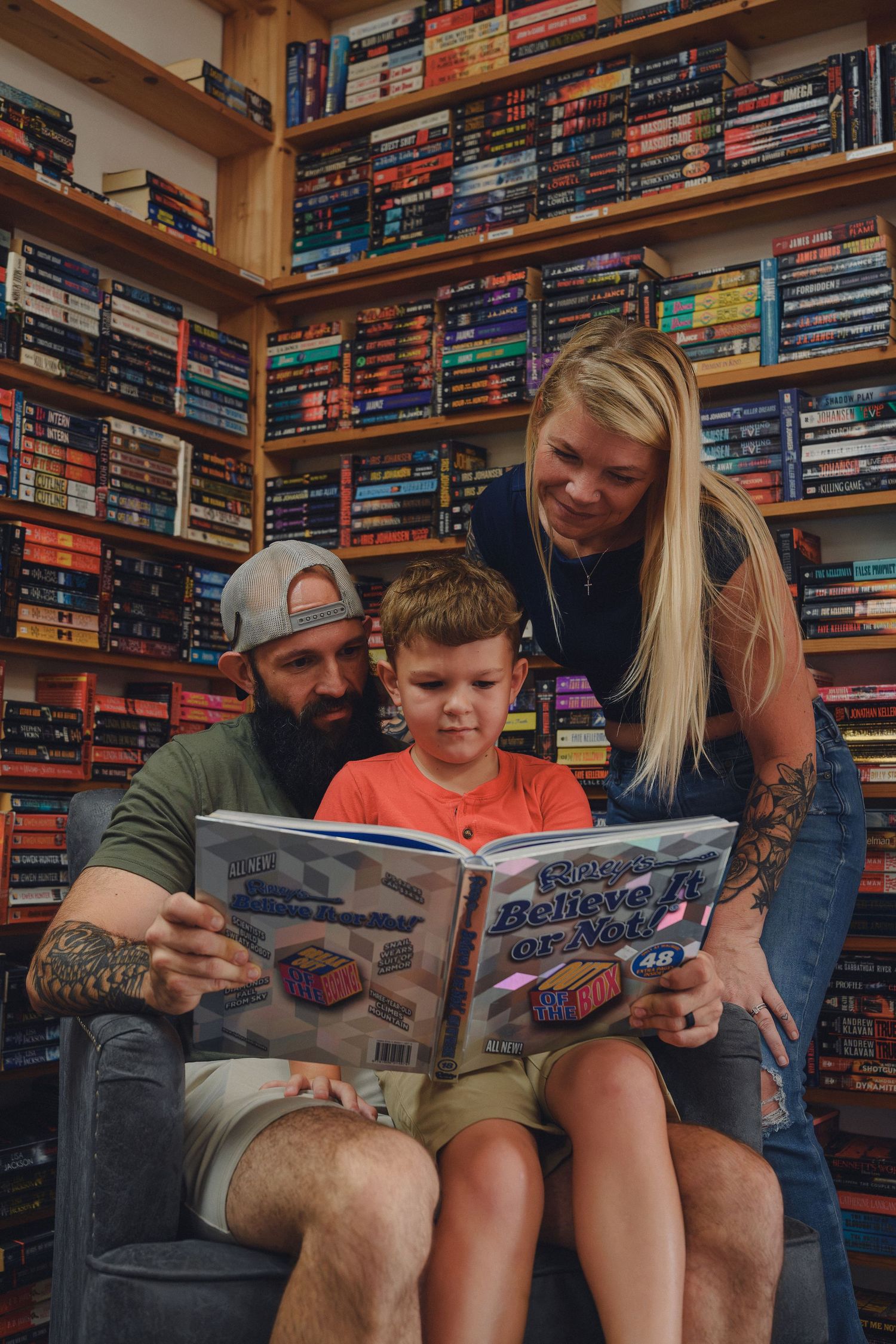 Family reading Ripley's Believe It or Not book together in a library with colorful bookshelves.
