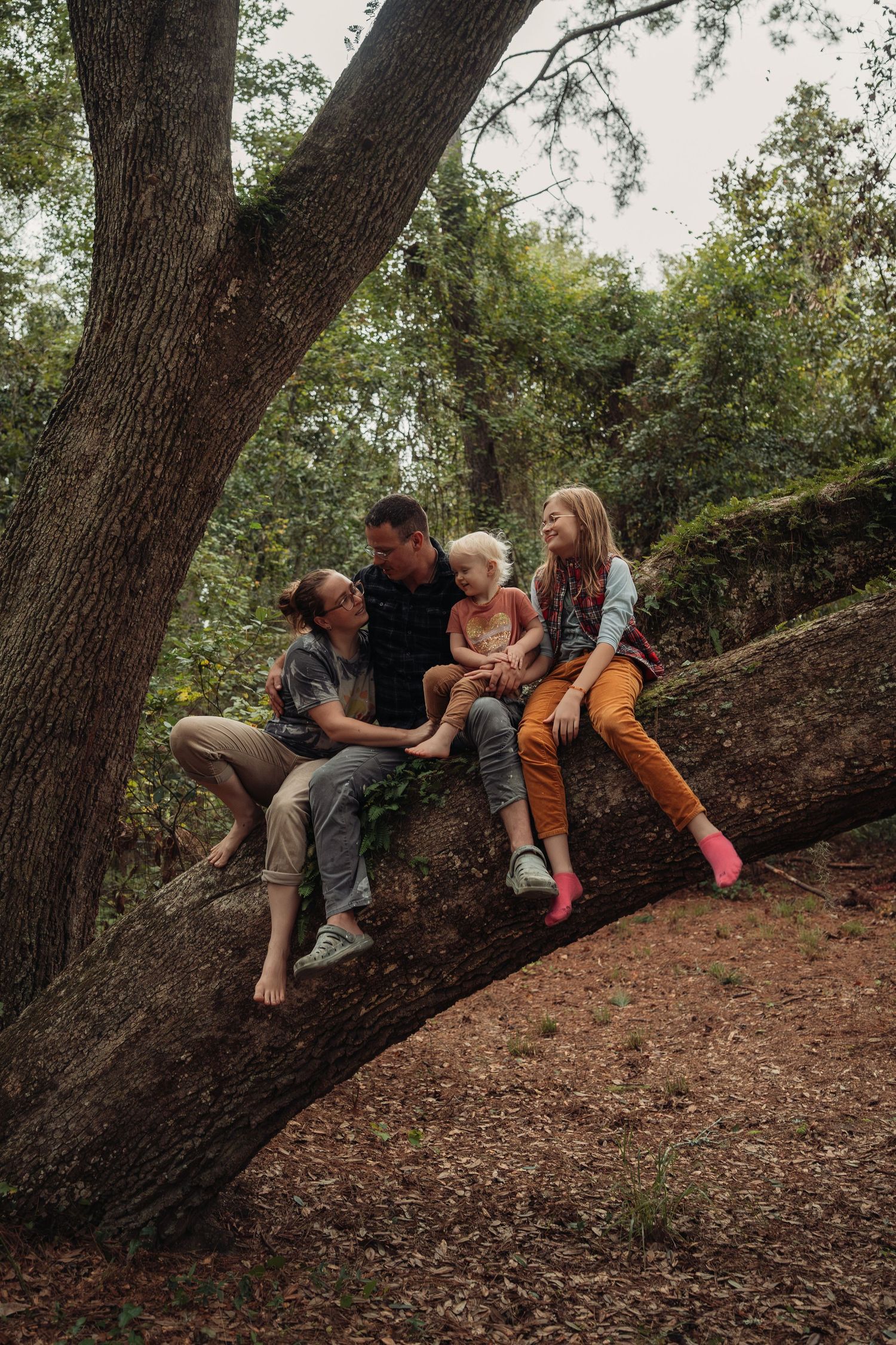 Family of four sitting together on a fallen tree trunk in a lush green forest, smiling and enjoying nature.