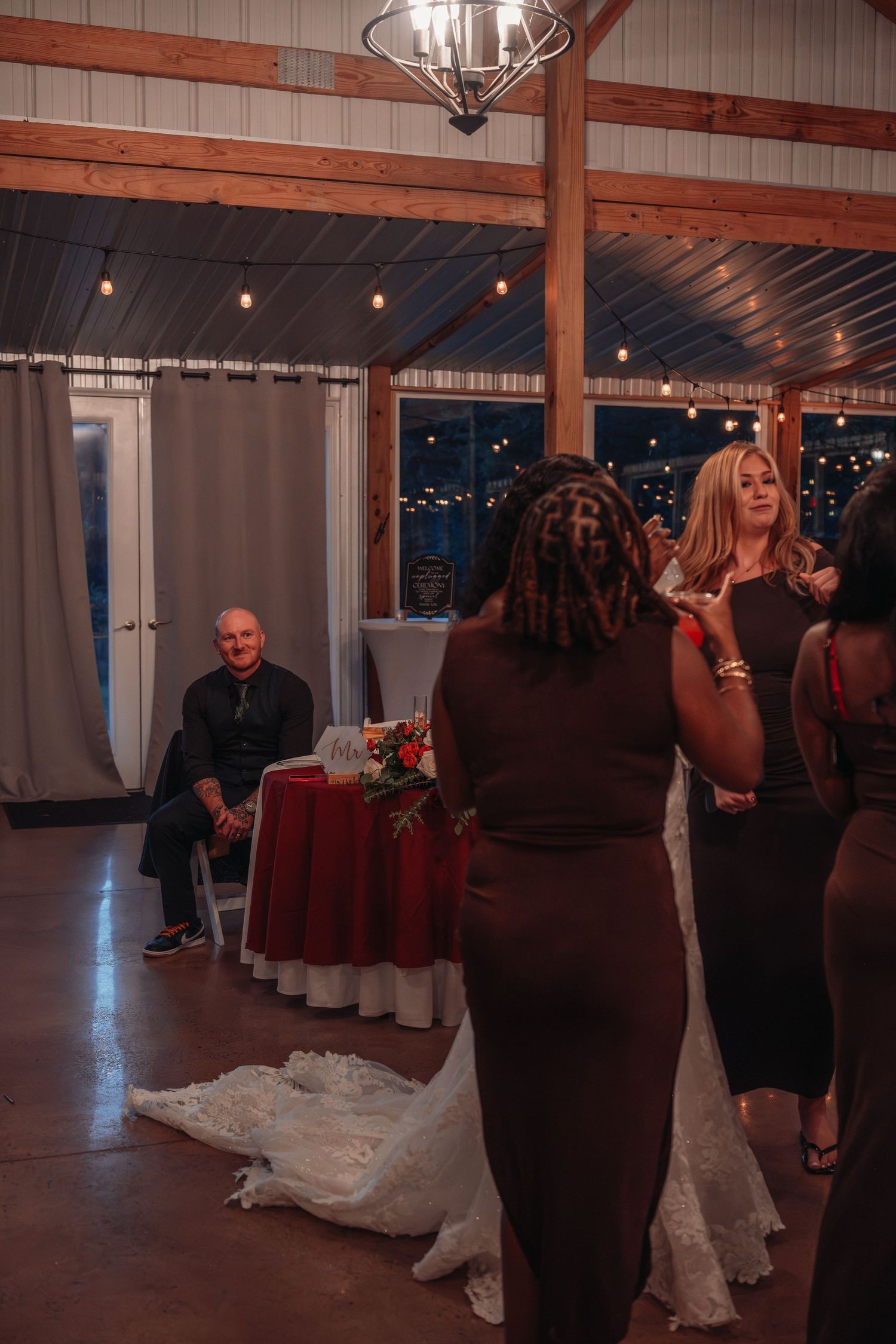 Guests gather on the dance floor during a wedding reception in a rustic barn venue with string lights.