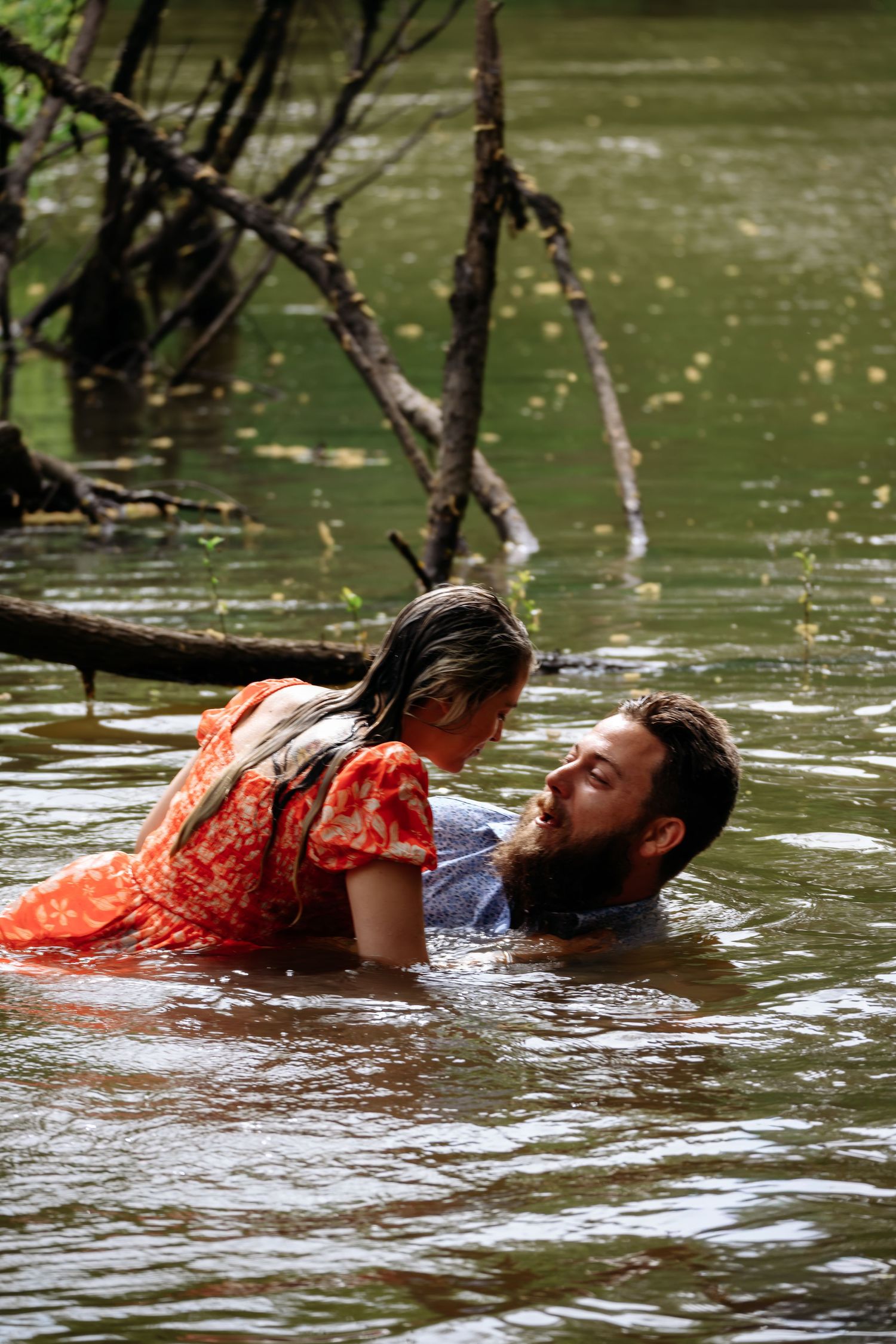Couple laughing and playing together while submerged in a peaceful forest river.