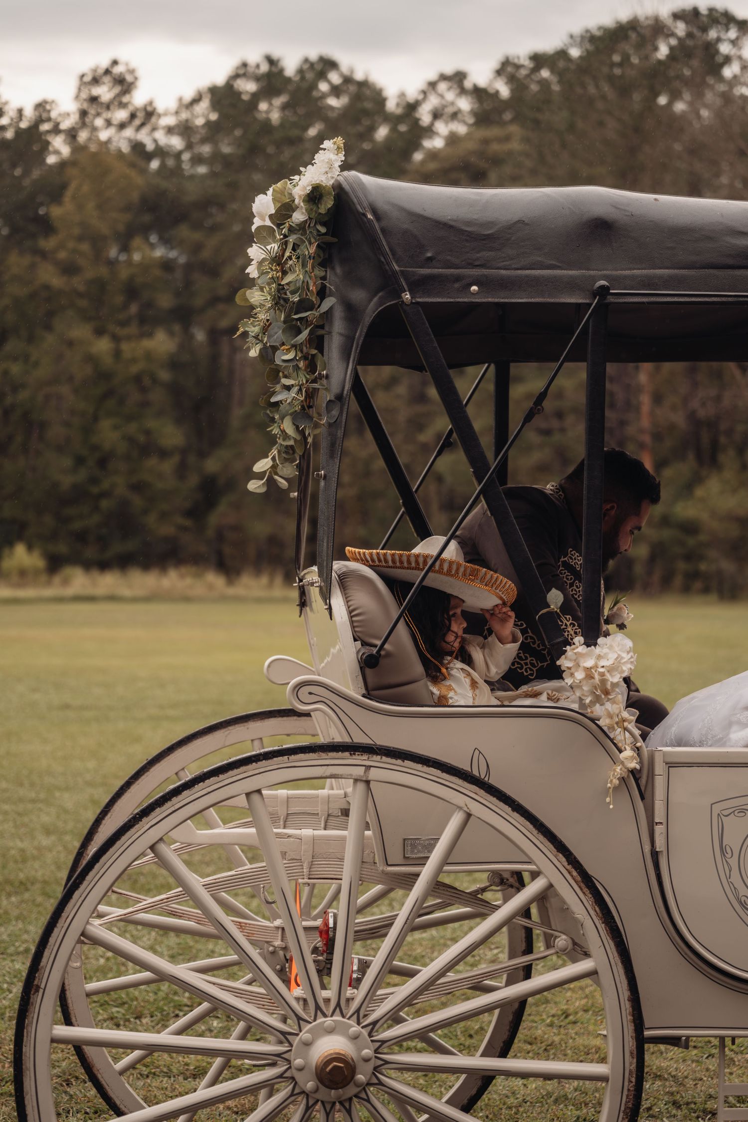 Elegant white horse-drawn wedding carriage adorned with white flowers and greenery garlands on a lush green lawn.