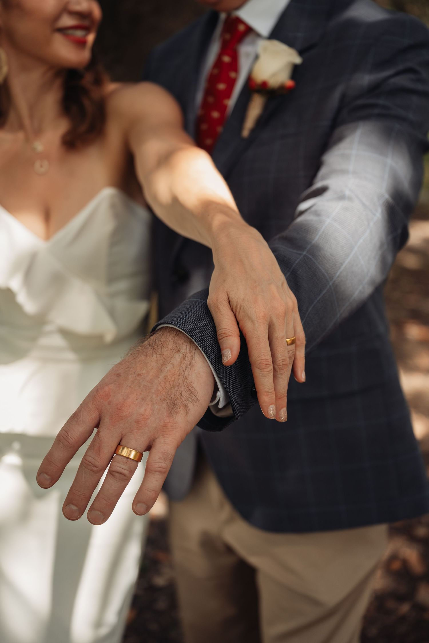 Newlyweds display their matching gold wedding bands side by side in a close-up outdoor portrait.