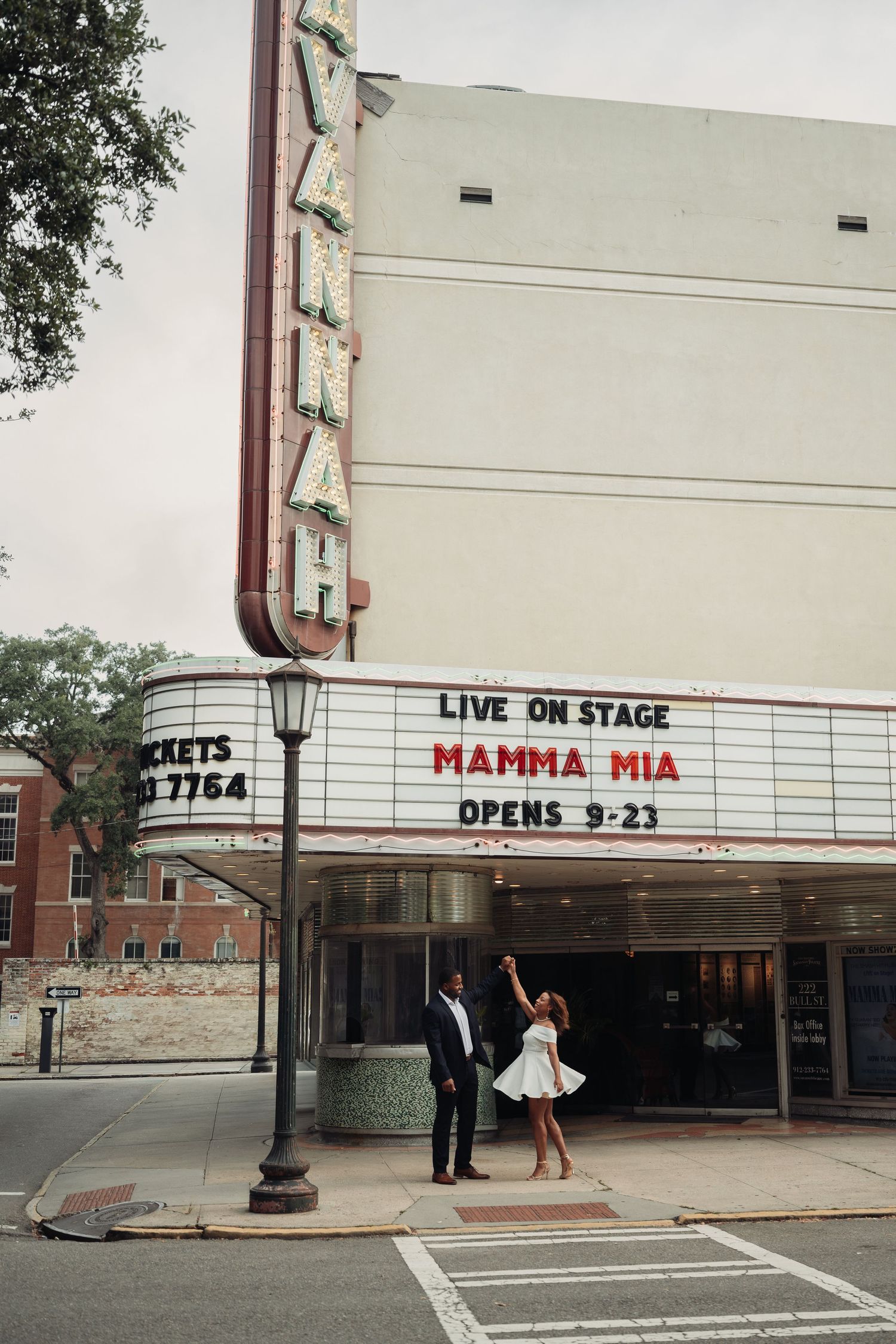 Couple dancing playfully outside Savannah theatre marquee advertising Mamma Mia live on stage.