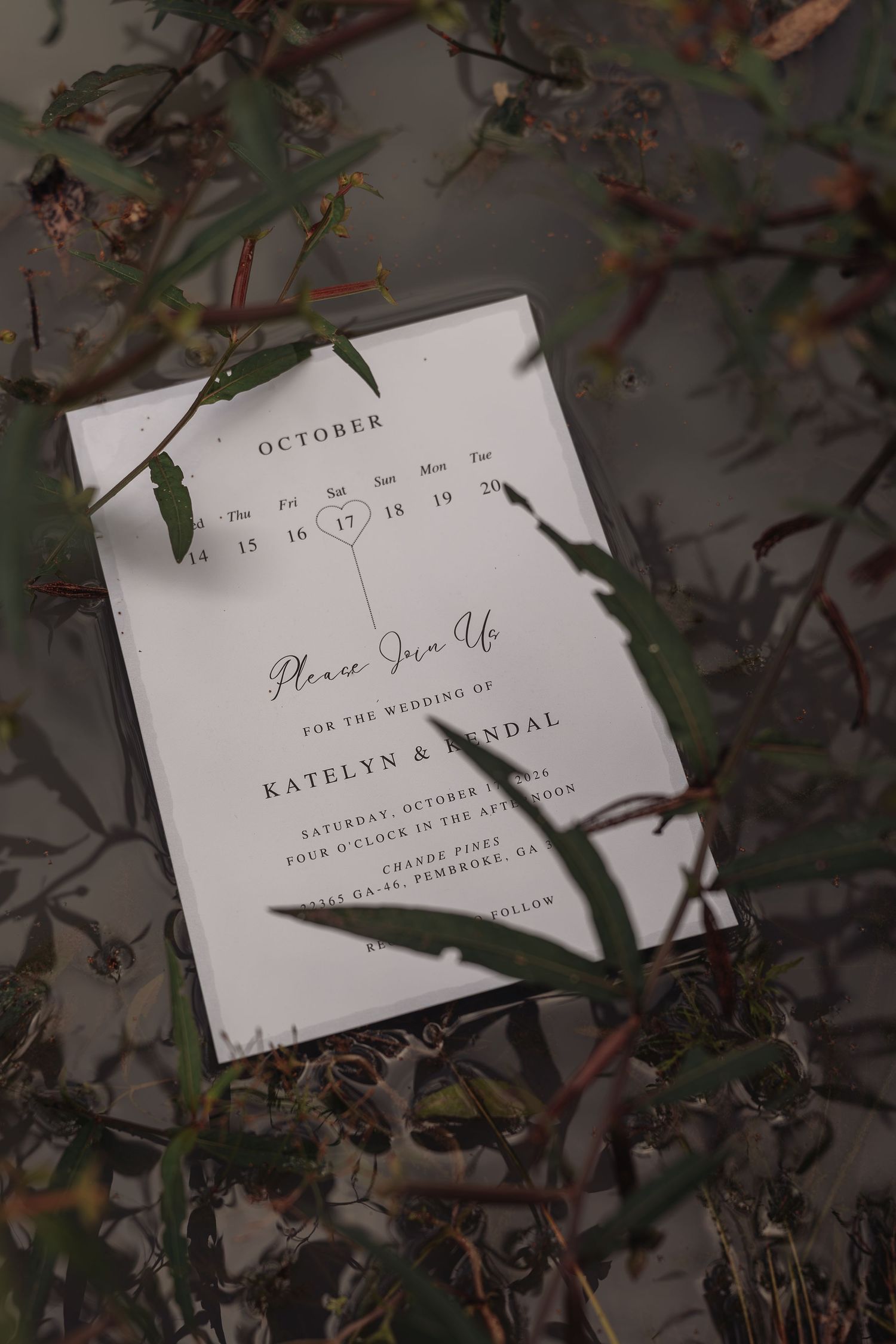 Elegant October wedding invitation for Katelyn and Kendal with a heart on the calendar, framed by dark green leaves and branches.