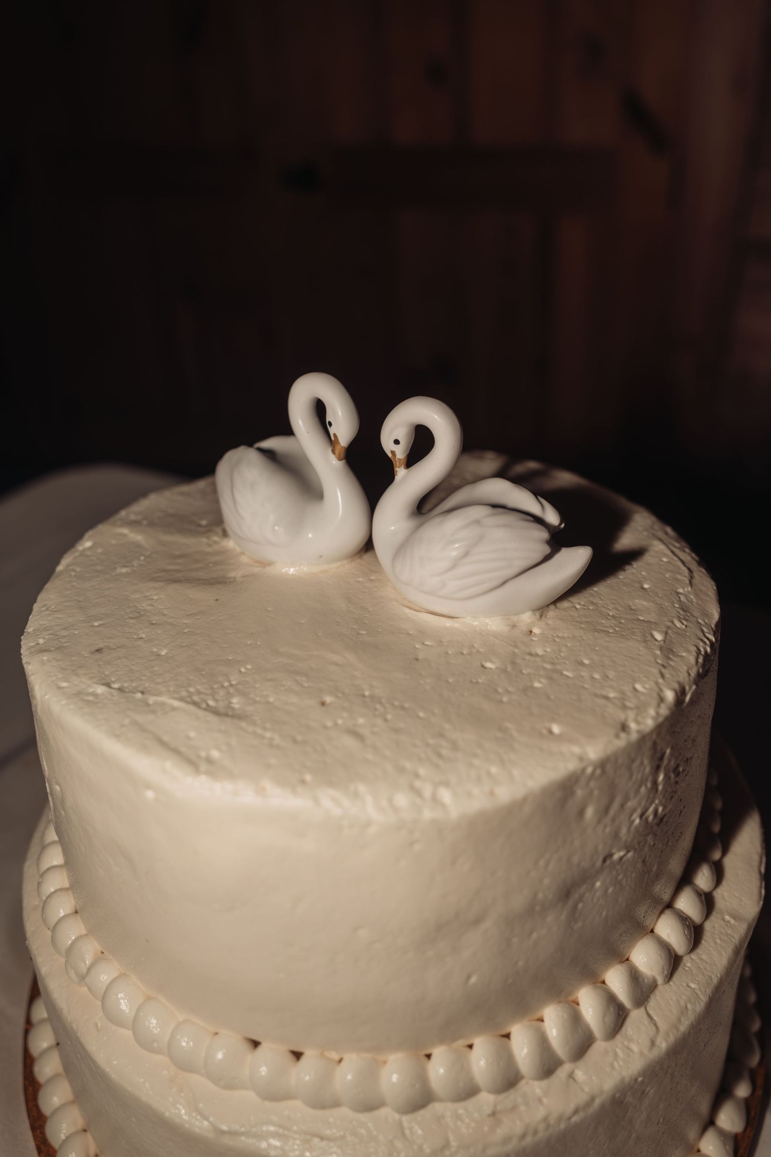 White wedding cake with two elegant swan figurines on top, symbolizing love and unity for a romantic celebration.