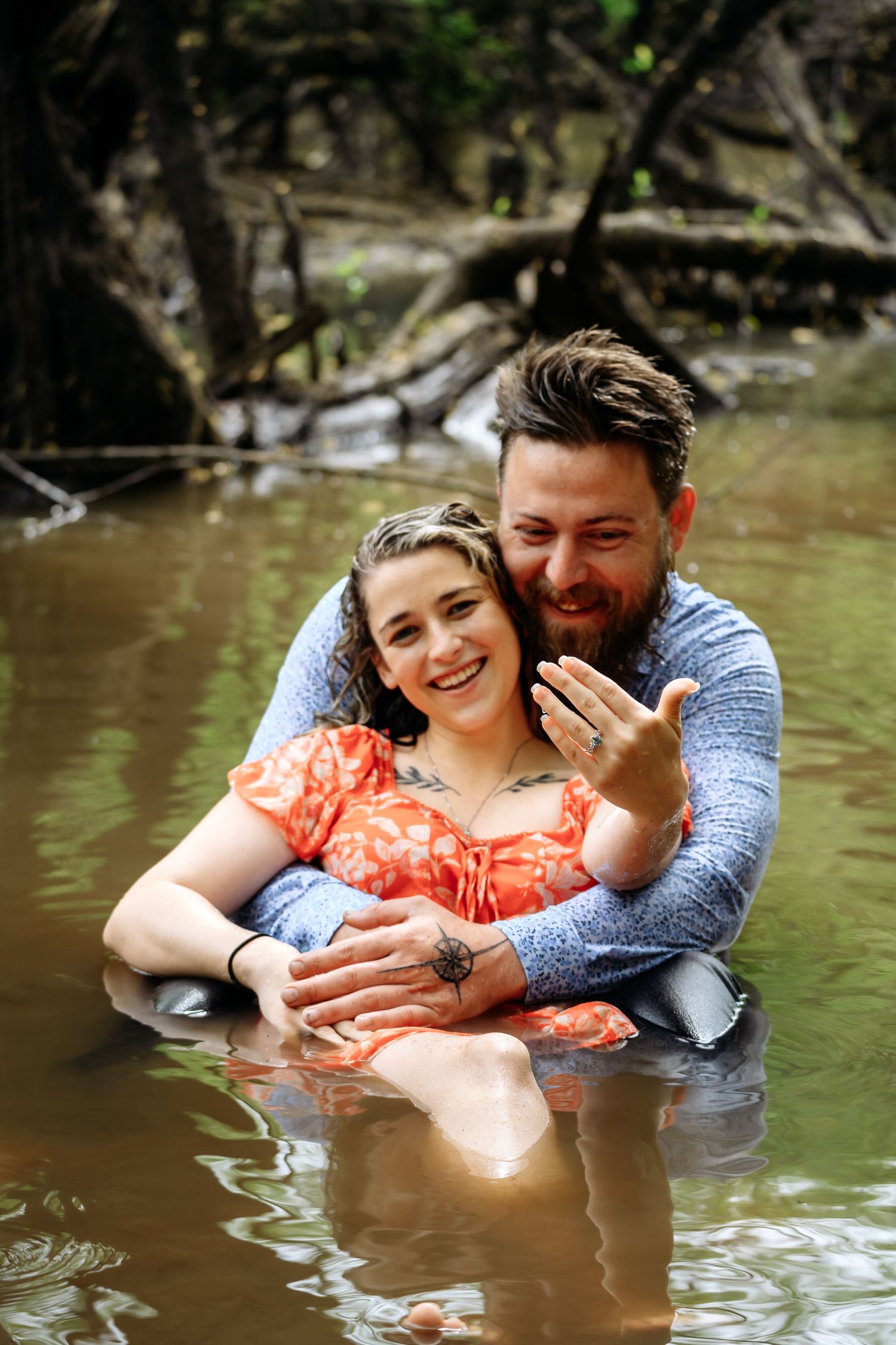 Couple embracing and smiling in a creek during an engagement photo session outdoors.