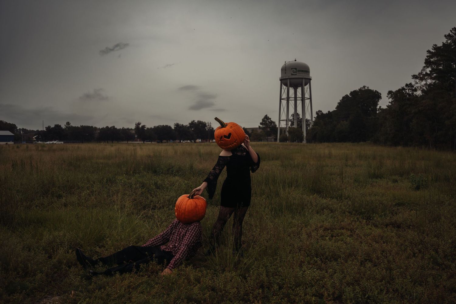 Two children in Halloween costumes holding pumpkins in a dark field with a water tower in the background.