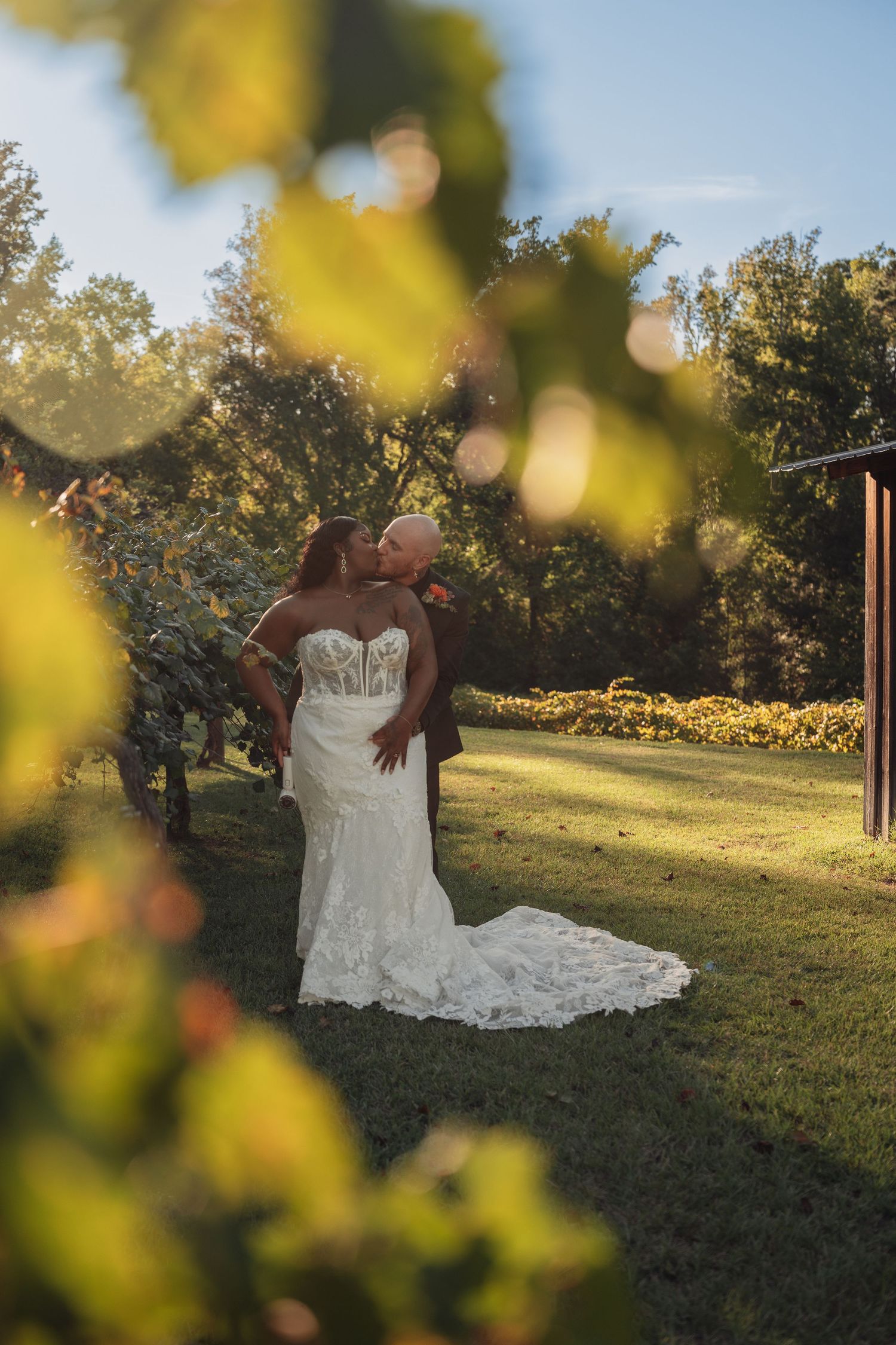 Couple kissing in lush garden framed by green leaves in warm golden sunlight.