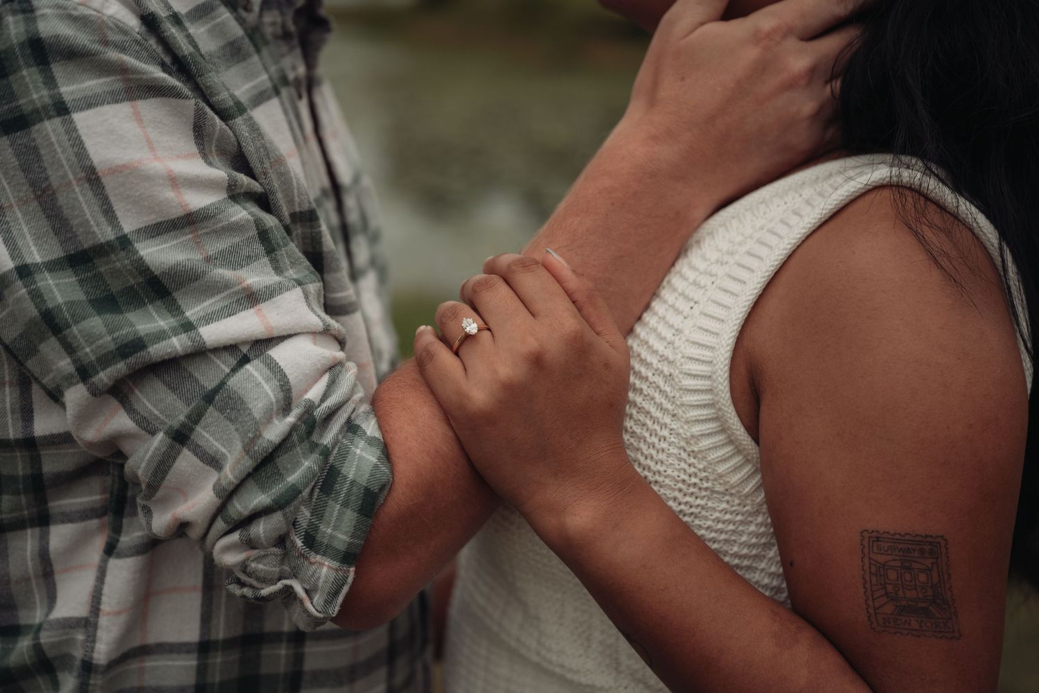 Close-up of a couple embracing, woman wearing an engagement ring and small tattoo on her arm, man in plaid shirt.