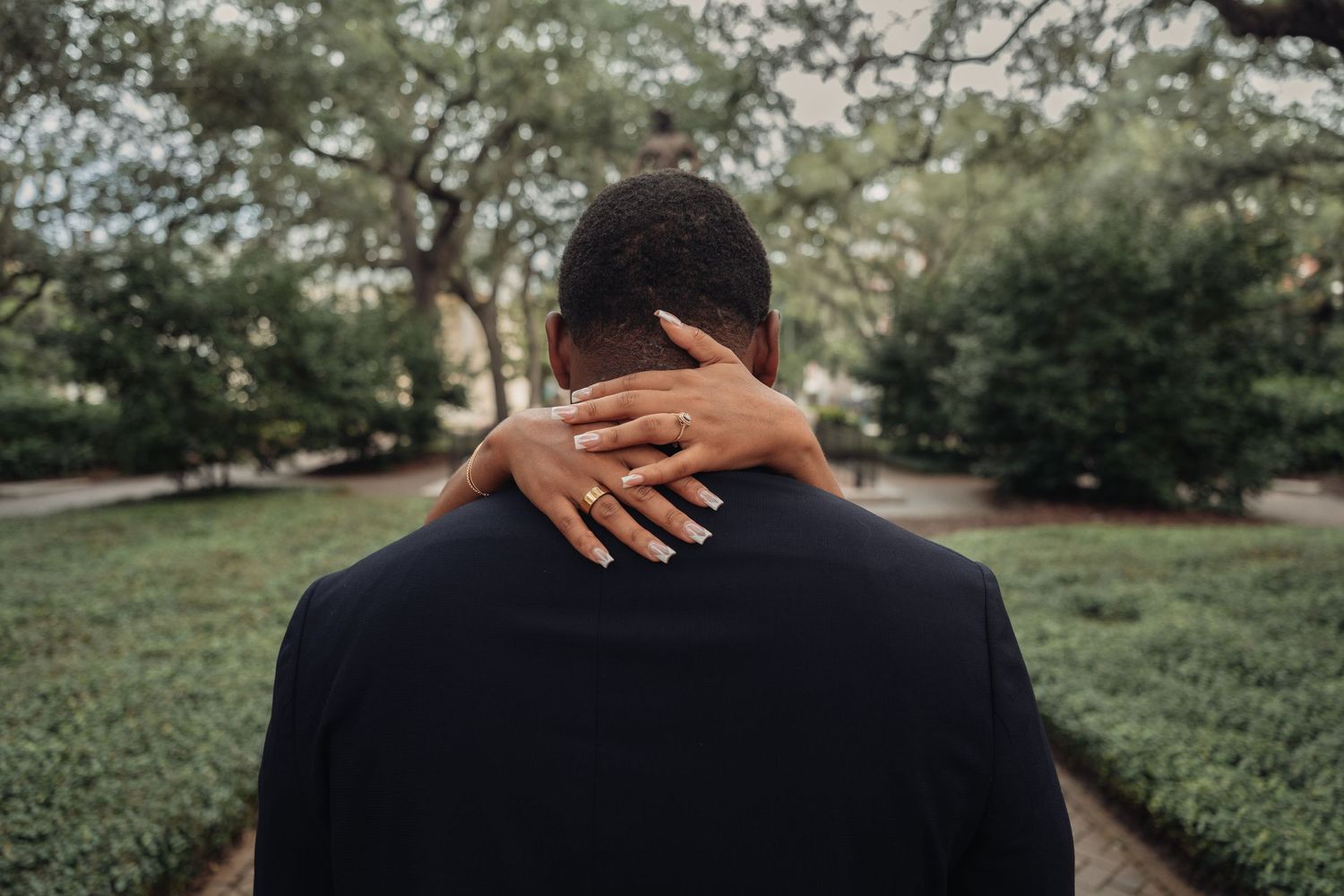 Close-up of woman's hand with manicured nails resting on man's navy suit jacket from behind.