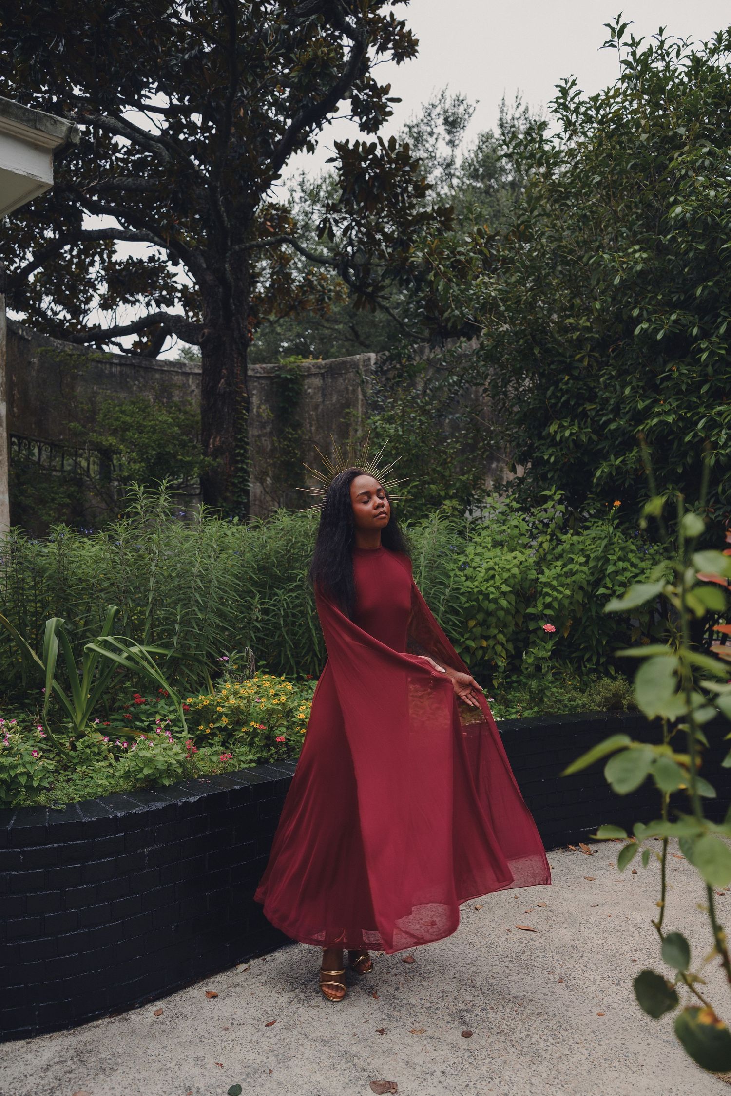 A woman in a flowing red maxi dress twirls gracefully in a lush green garden setting.