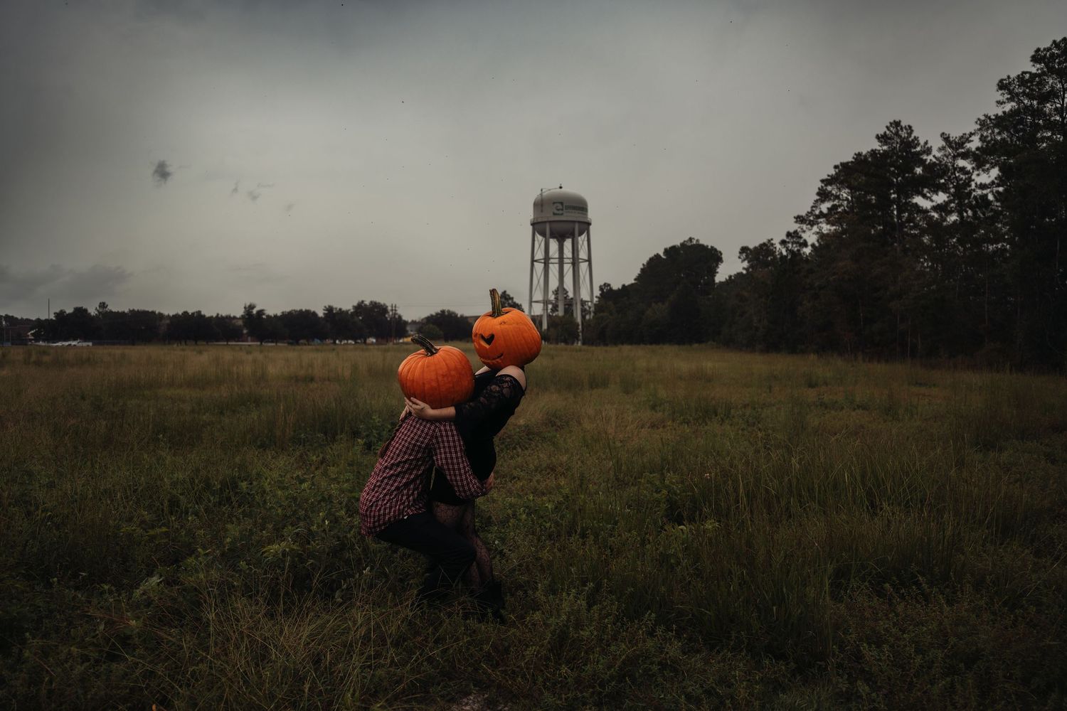 Child carrying large pumpkins in a misty field with a water tower in the background on a cloudy autumn day.