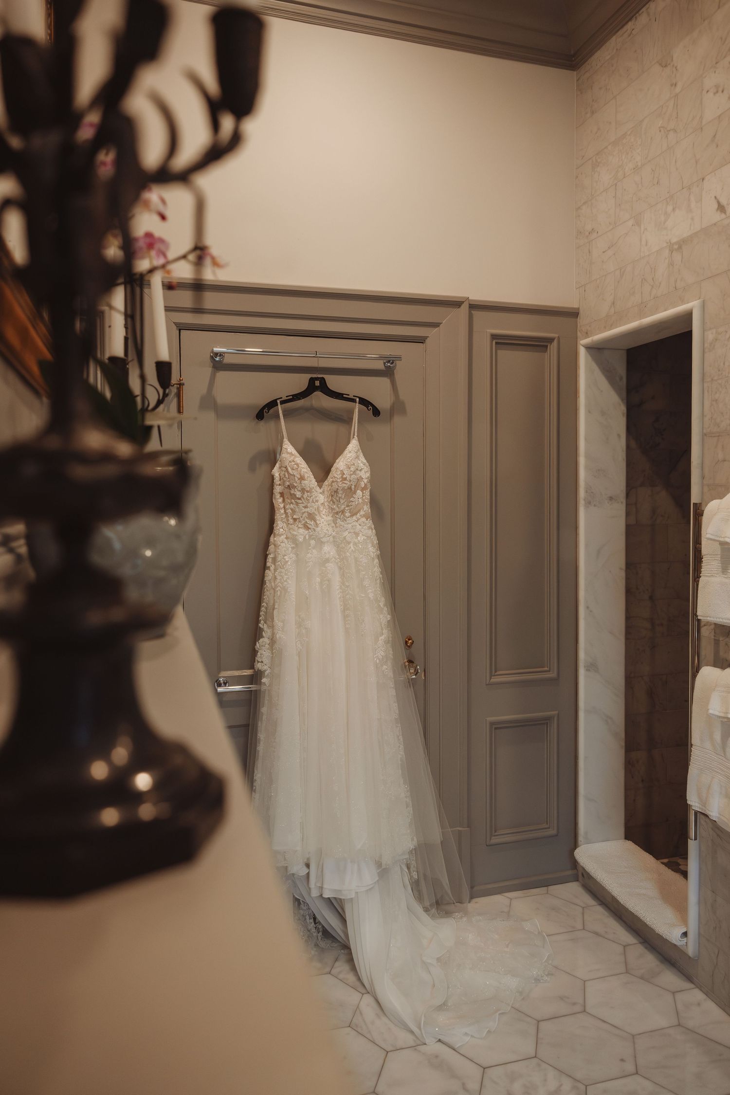 A delicate lace A-line wedding dress hanging on a hanger in an elegant bridal suite with marble floors.