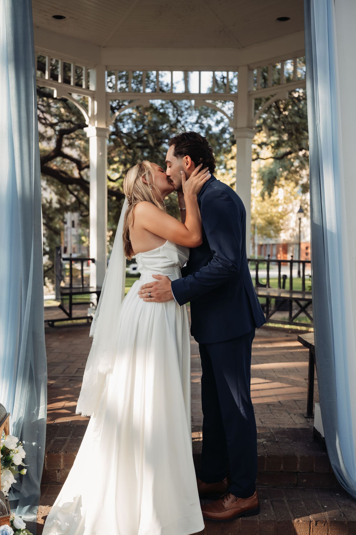 Bride and groom share their first kiss as newlyweds inside a white gazebo with blue draping.