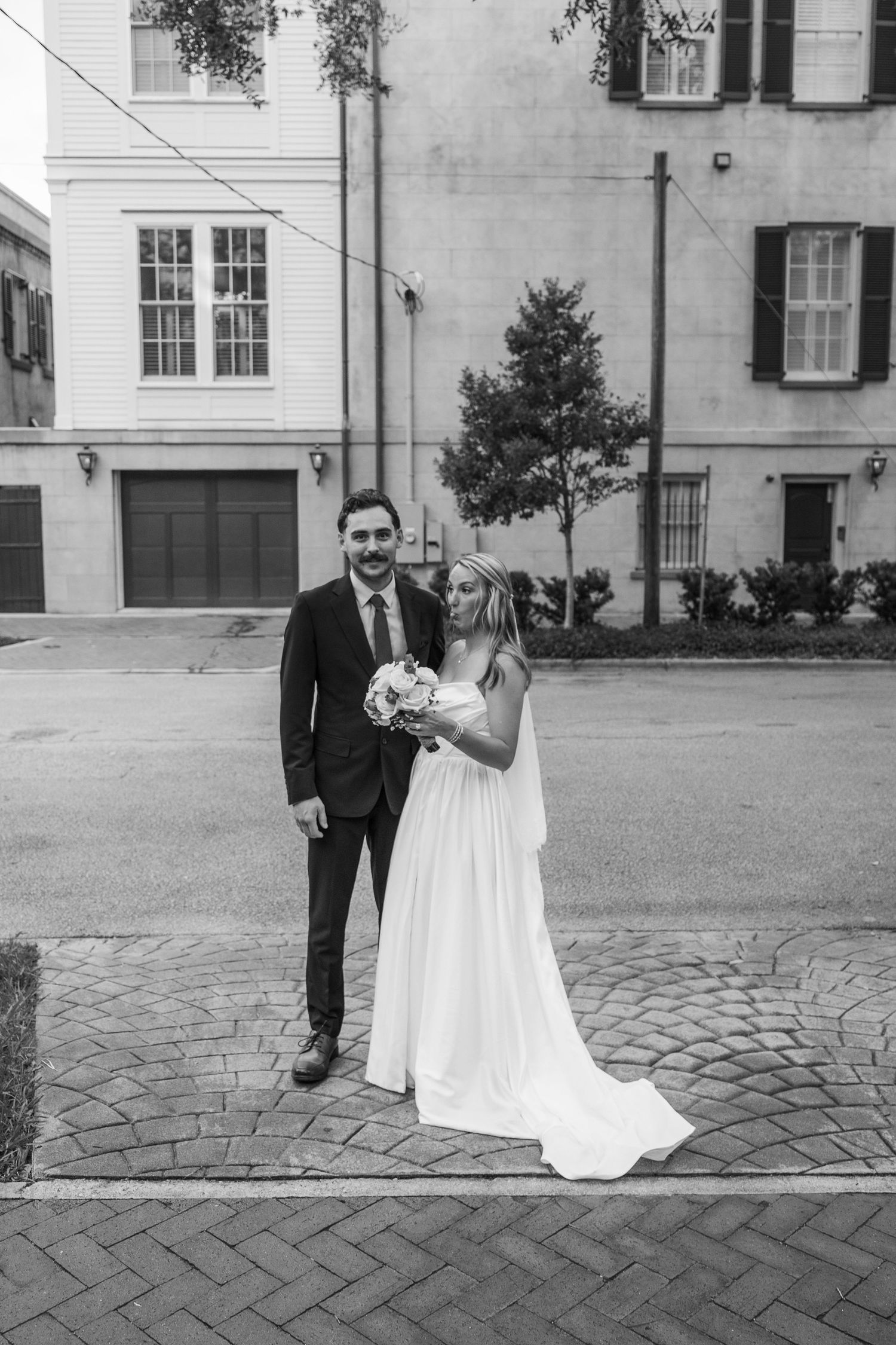 Black and white portrait of bride and groom standing on cobblestone street in historic district.