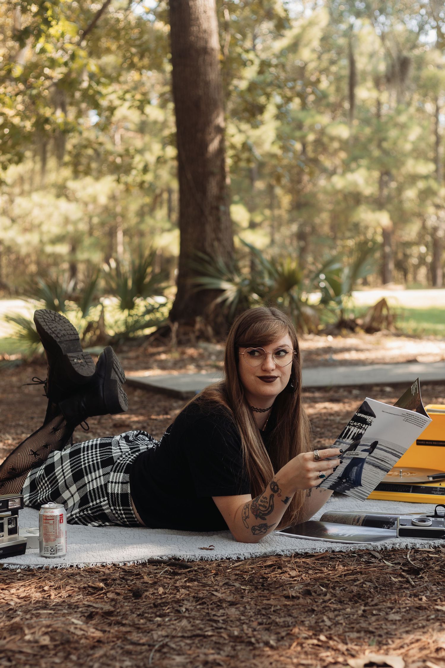 Young woman with tattoos lying on a blanket in a park reading next to a yellow typewriter.