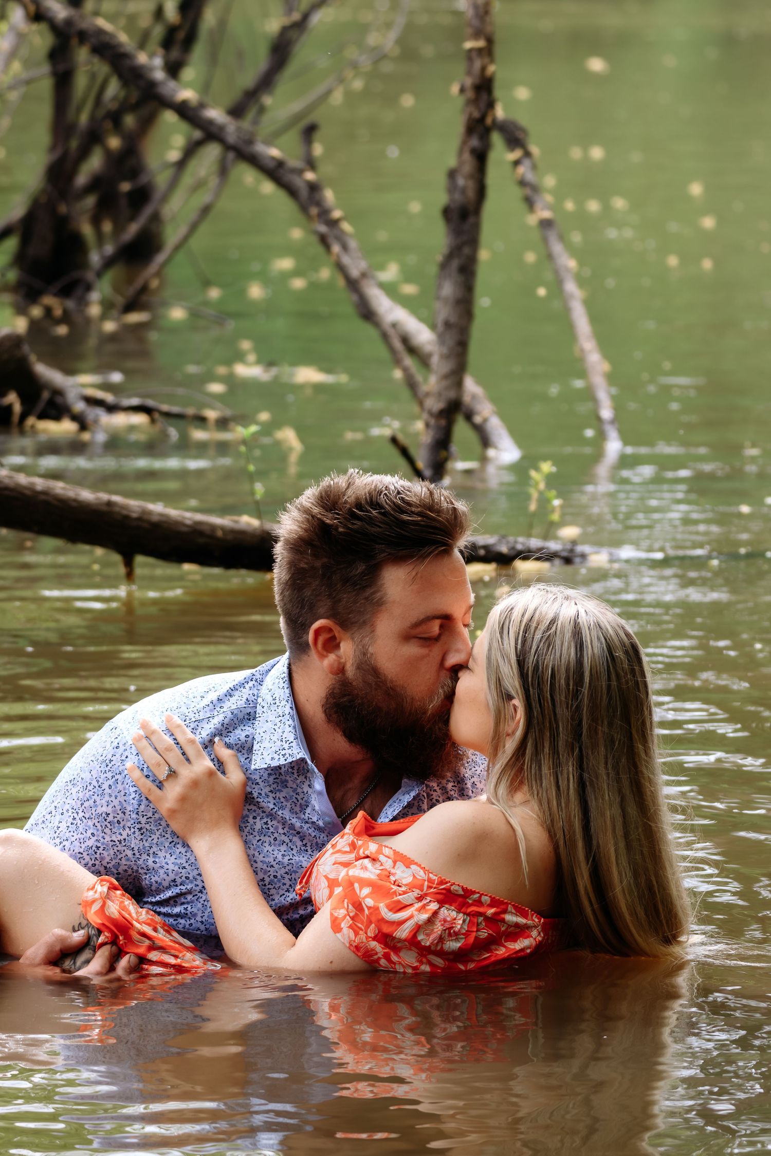 Engaged couple kissing romantically while standing in a shallow river in nature.
