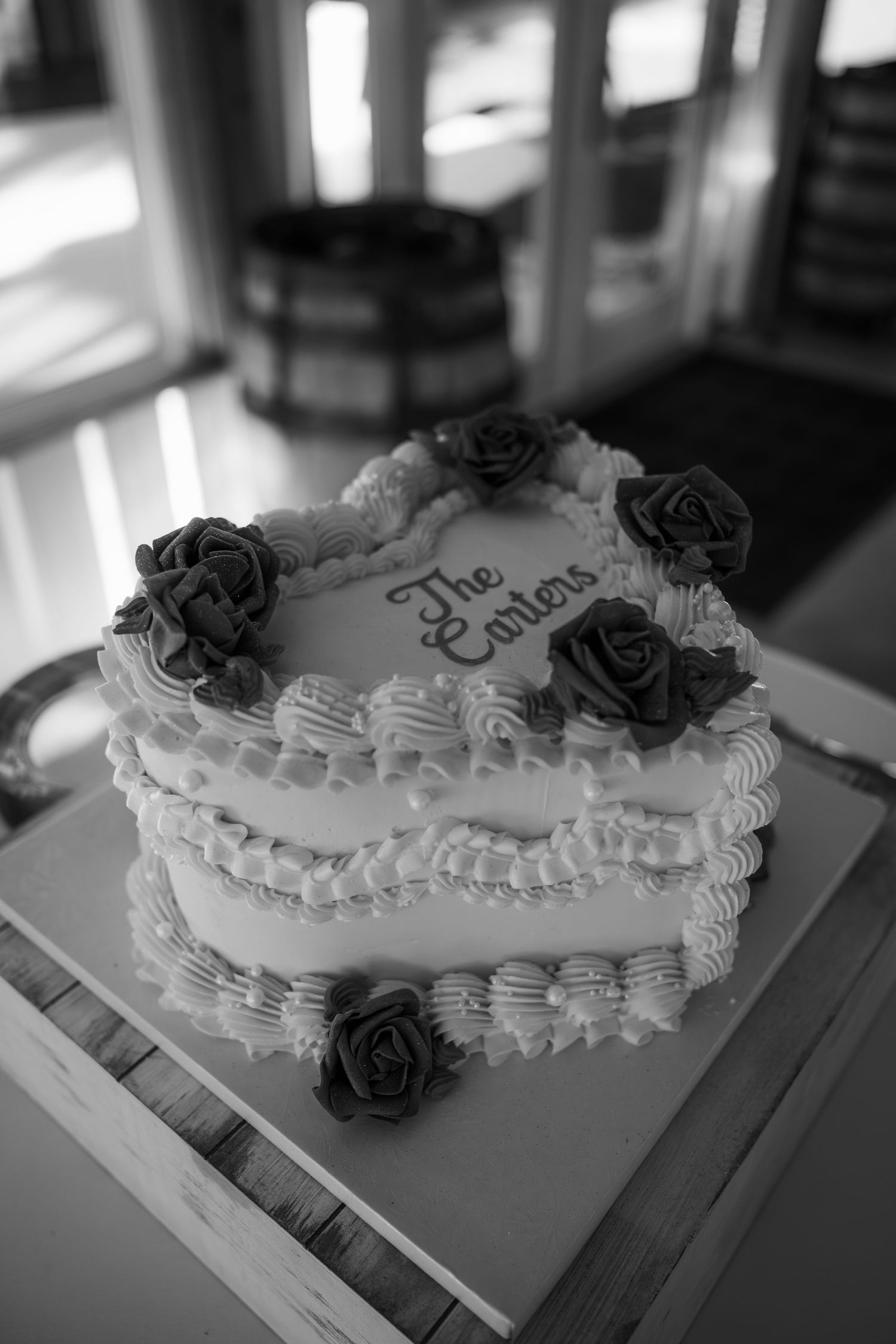 Black and white photo of a wedding cake decorated with roses inscribed with The Carters.