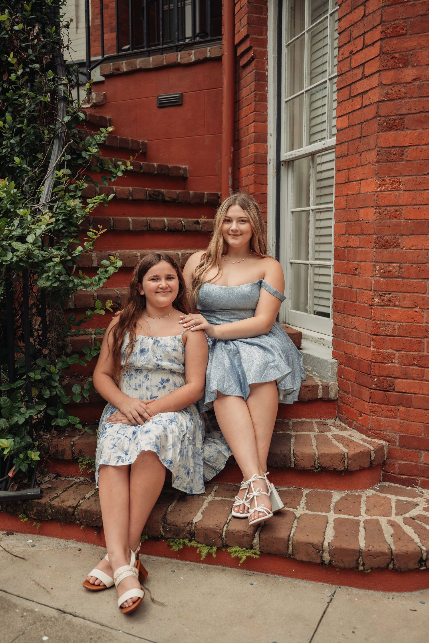 Two girls in blue dresses sitting on brick steps outside a red brick building.