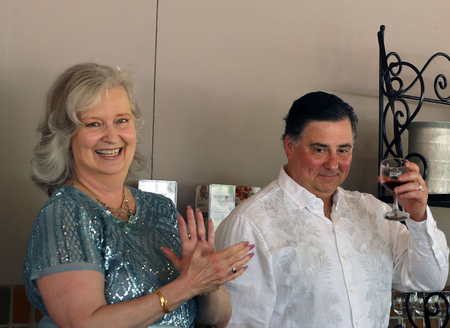 Woman laughing and clapping next to a man raising a glass of wine, candid party moment