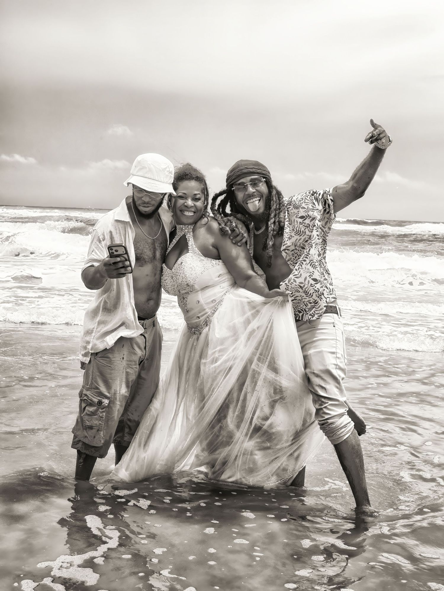 Woman in a flowing white dress laughs between two men on a Jacksonville beach as waves wash over their feet