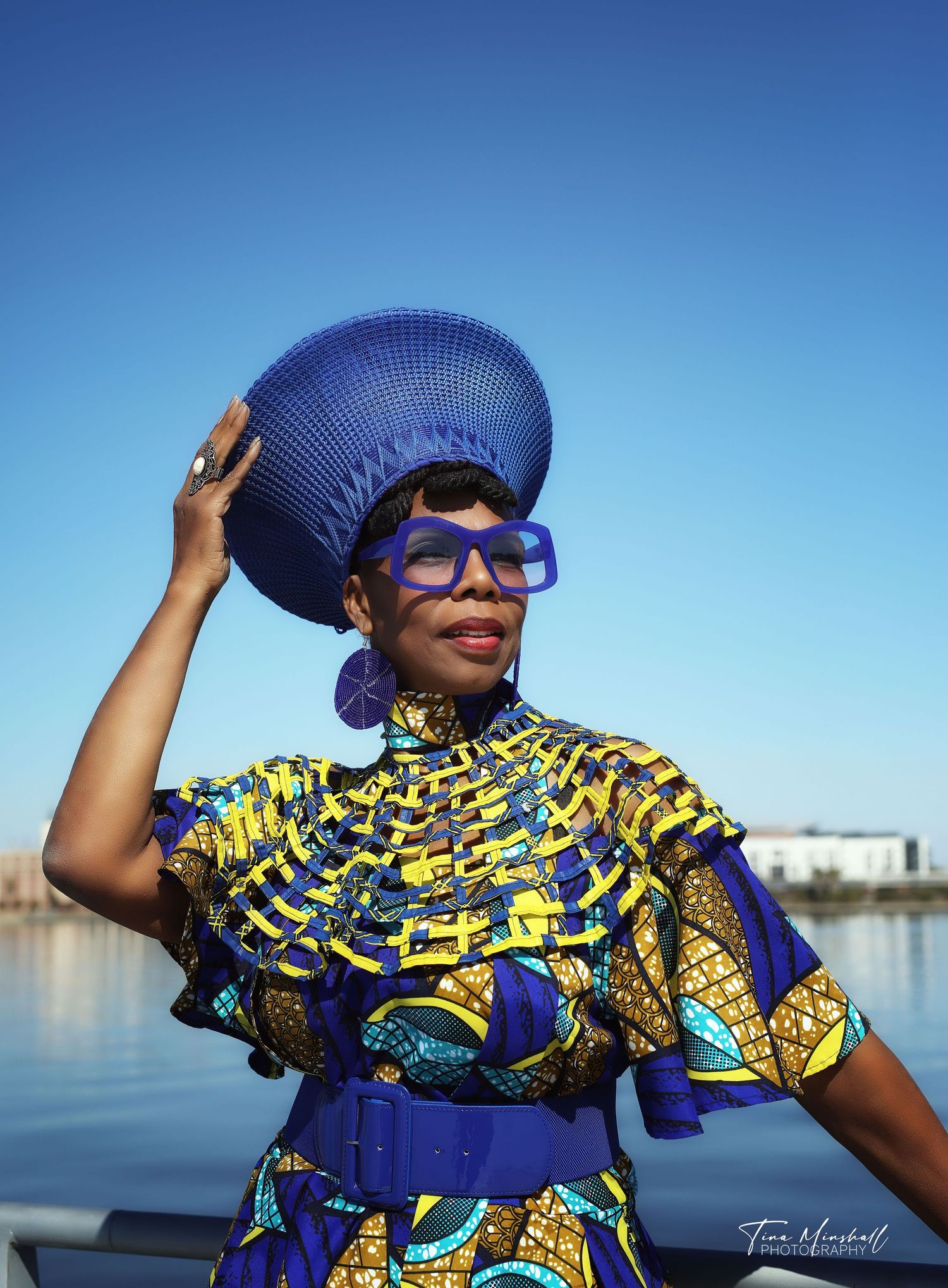 Woman in a vibrant blue and yellow African print dress and headwrap, confident portrait by the water