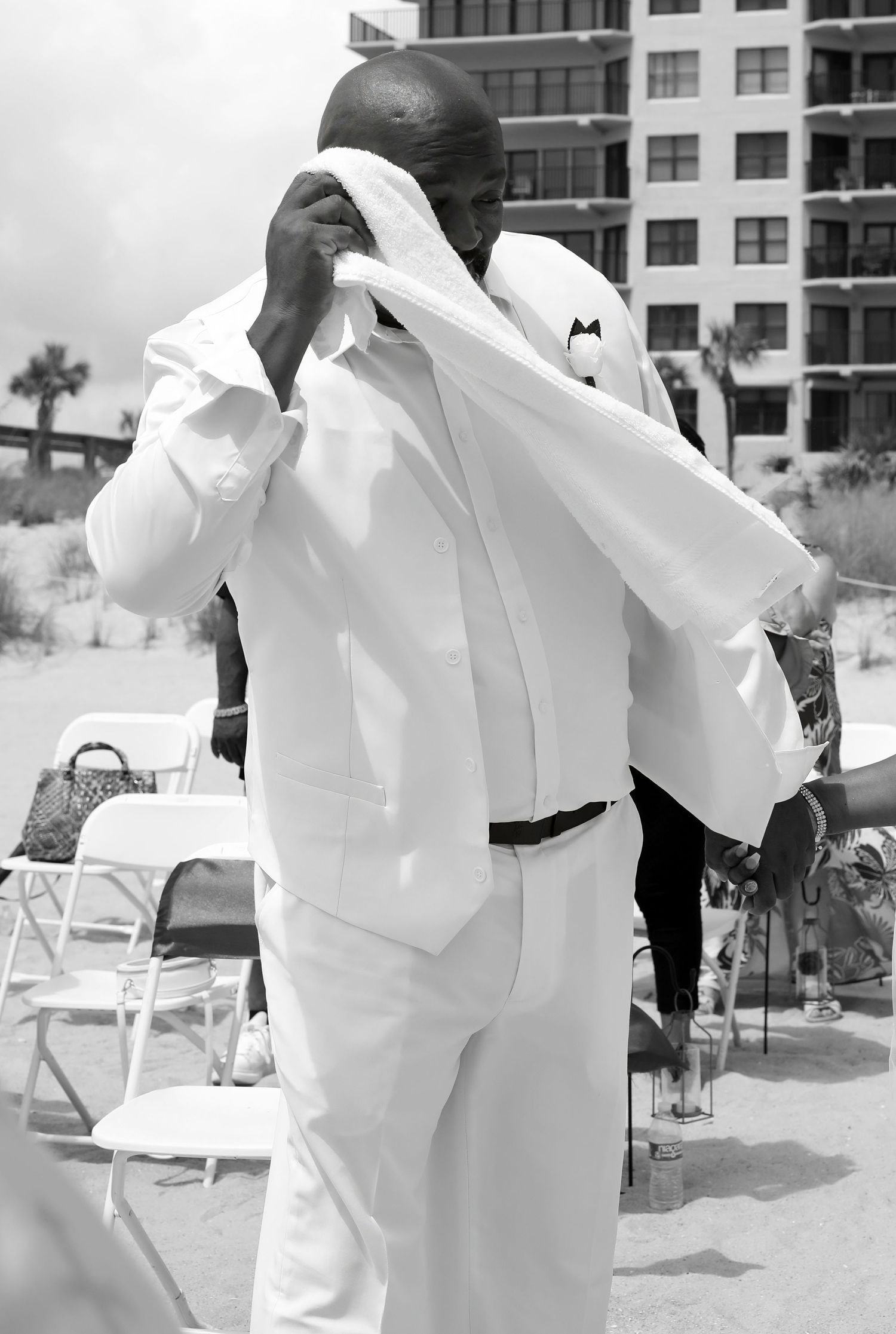 Black and white candid of a man wiping his face with a towel during an emotional beach wedding moment