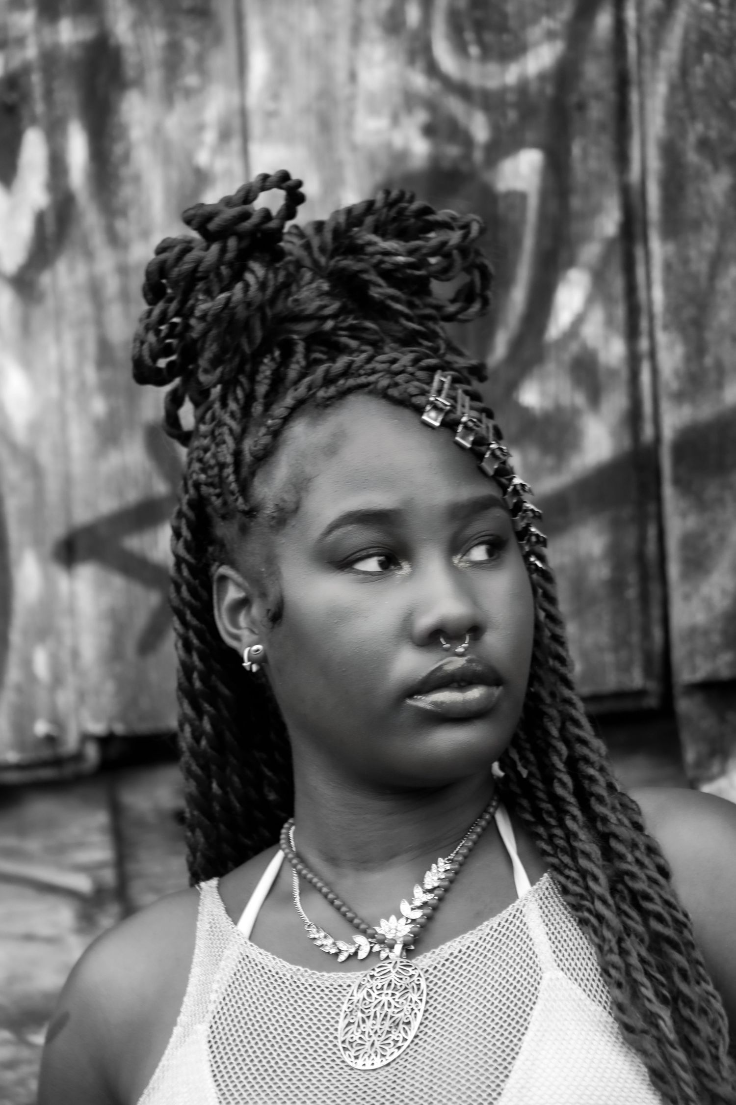 Black and white portrait of a woman with elaborate braided hair against a weathered wall