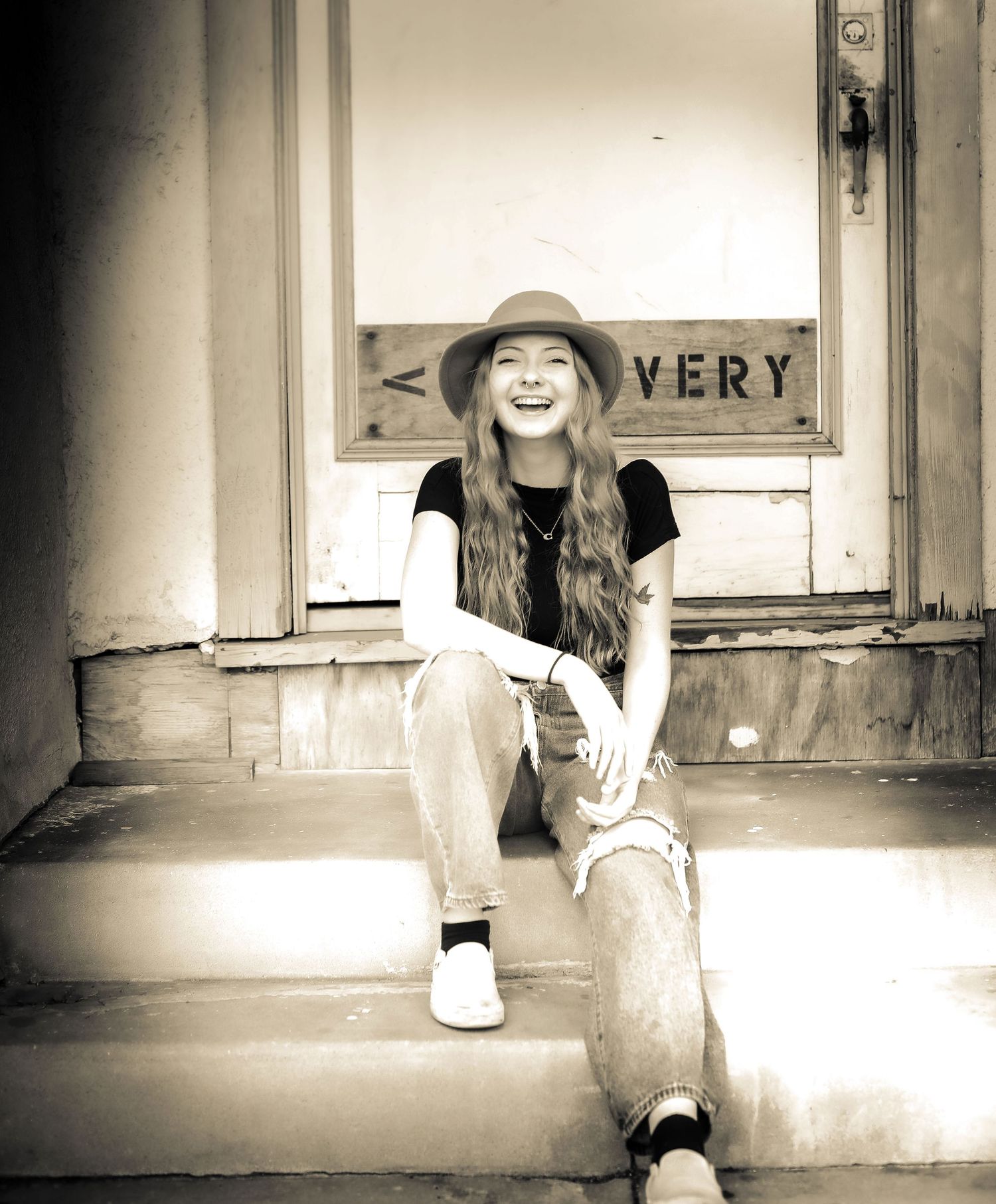 Sepia-toned portrait of a smiling woman sitting on the steps of a historic storefront