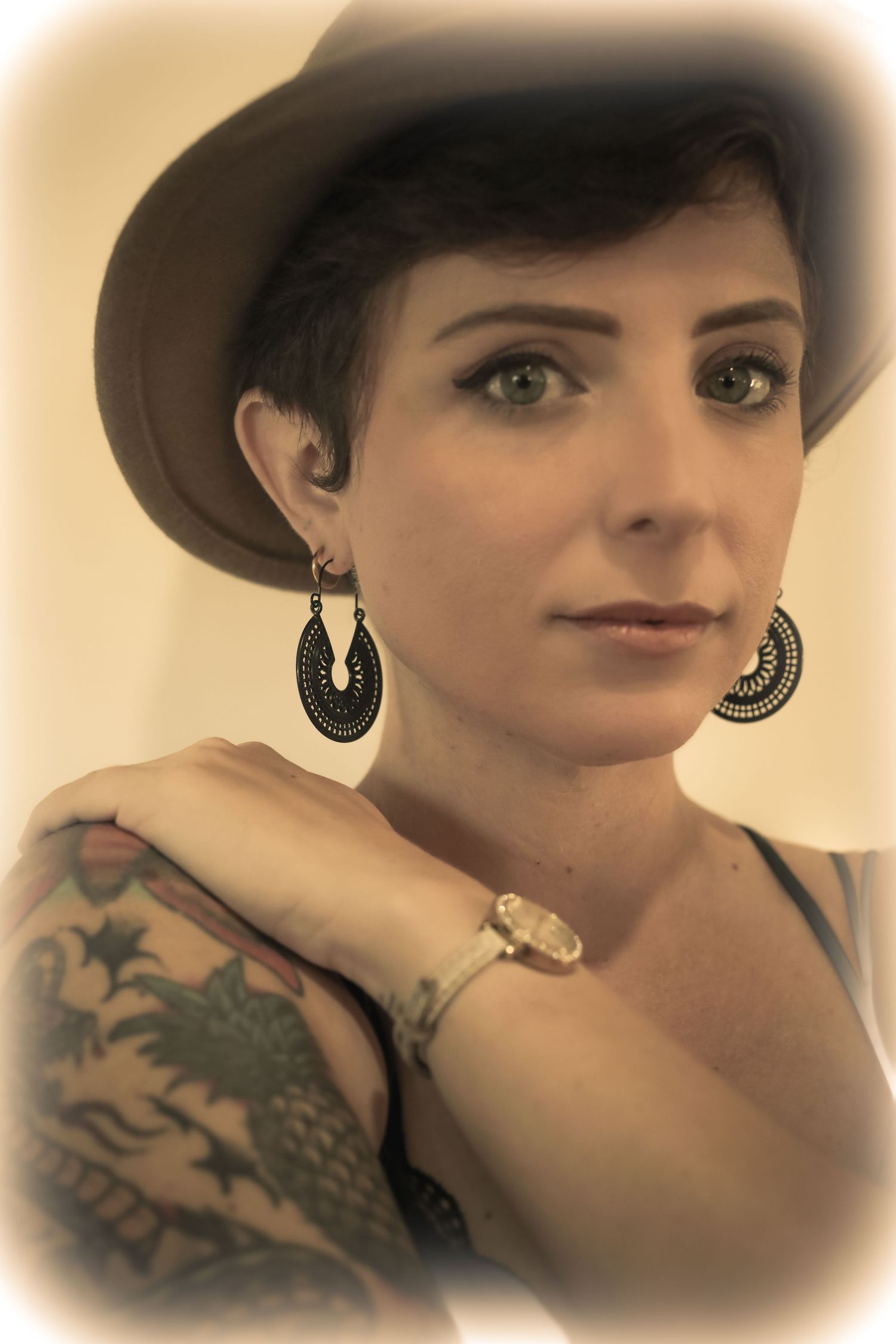 Close-up portrait of a woman with a pixie cut and wide-brim hat, warm sepia tone