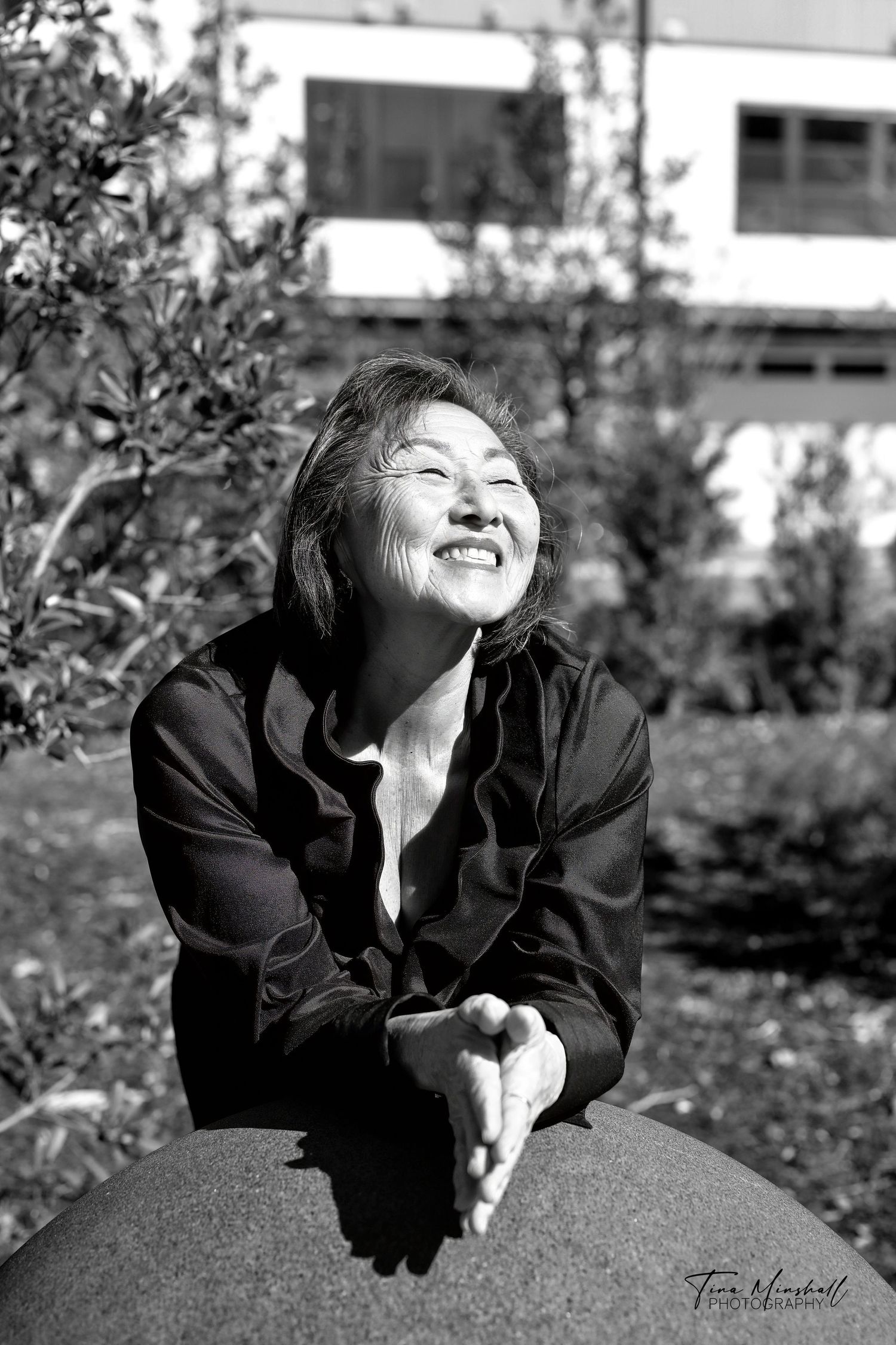 Black and white portrait of a woman laughing joyfully with her head tilted back, hands clasped