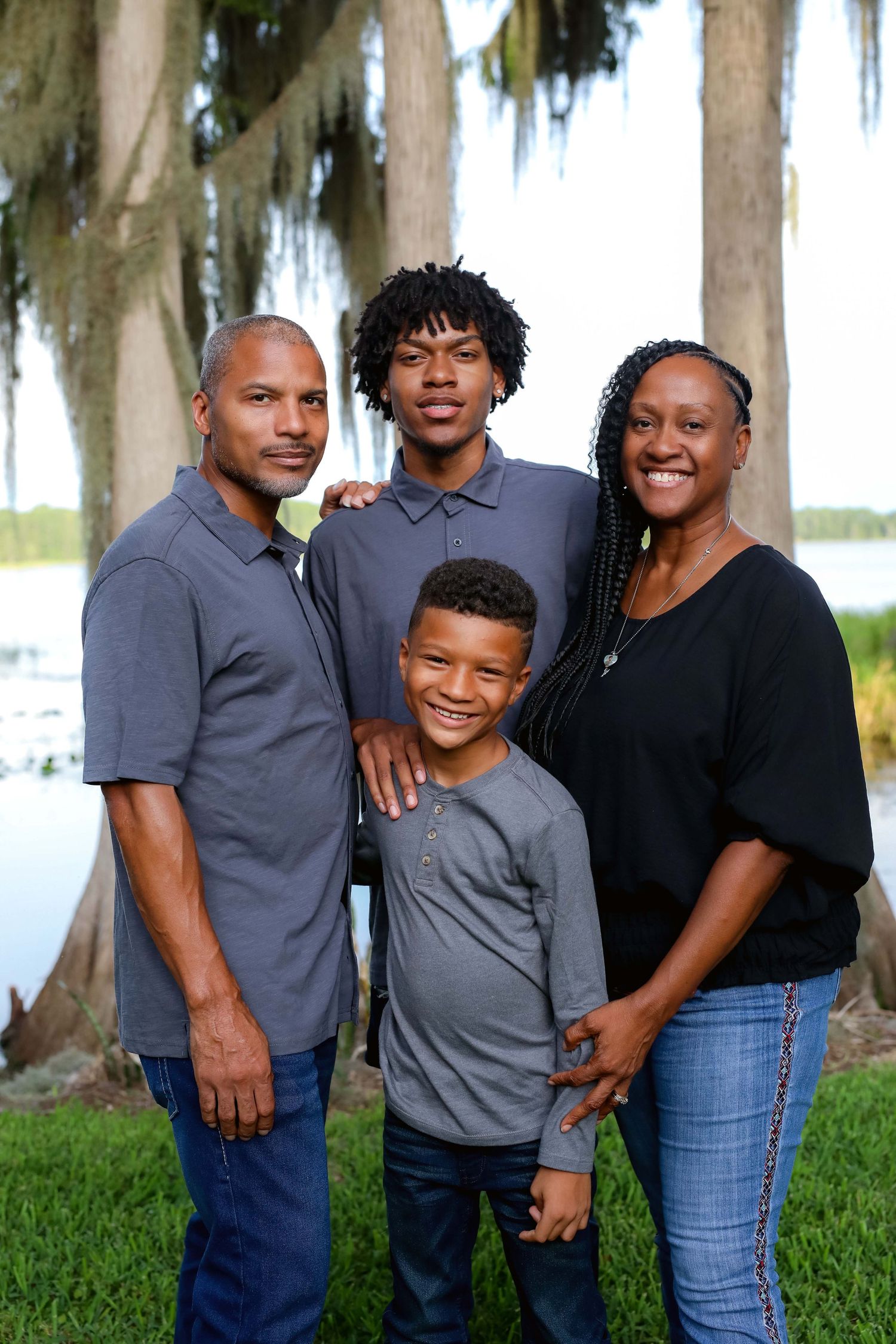 Family of four standing close together under moss-draped oak trees by the water
