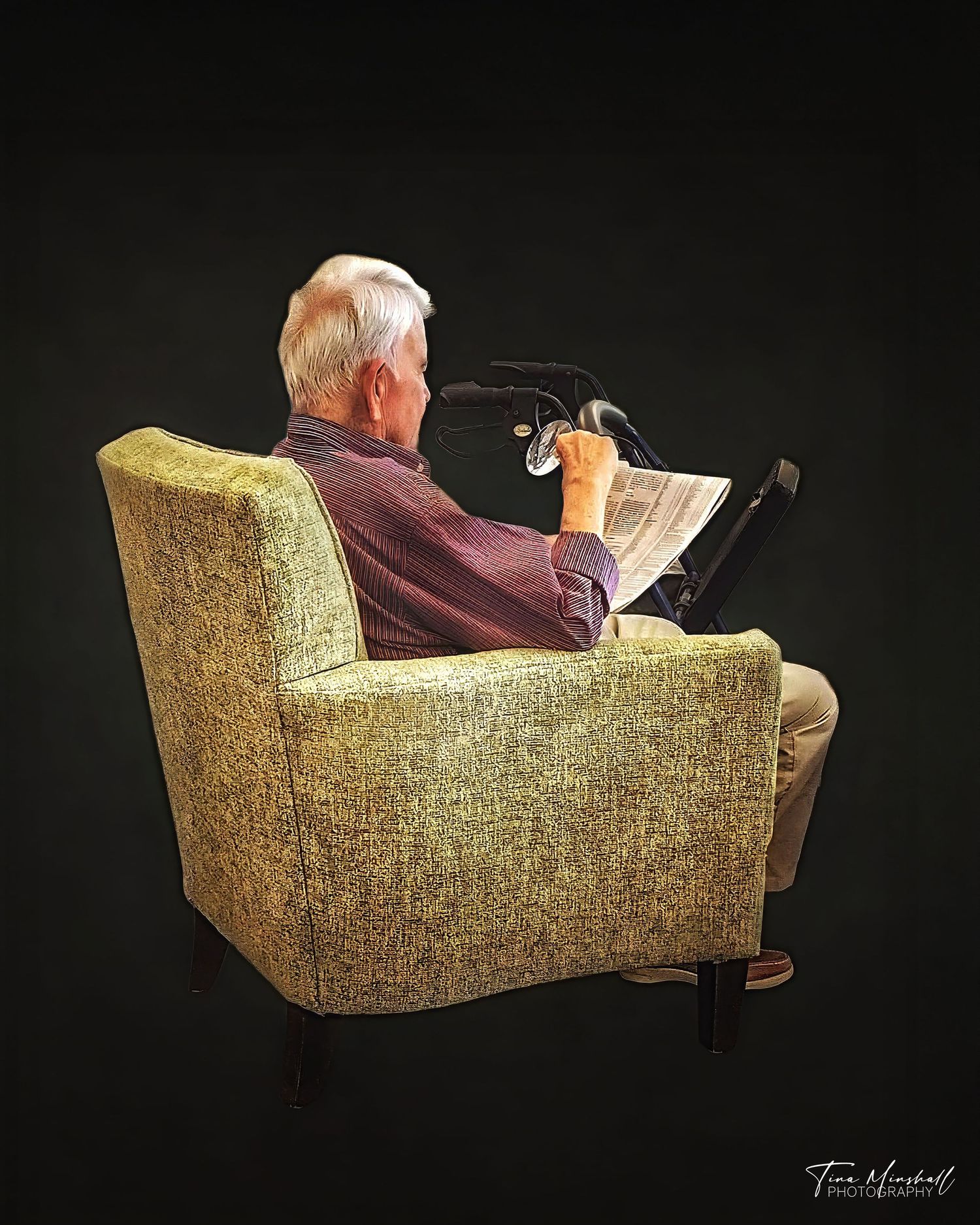 Black and white portrait of an older man reading a newspaper in an armchair