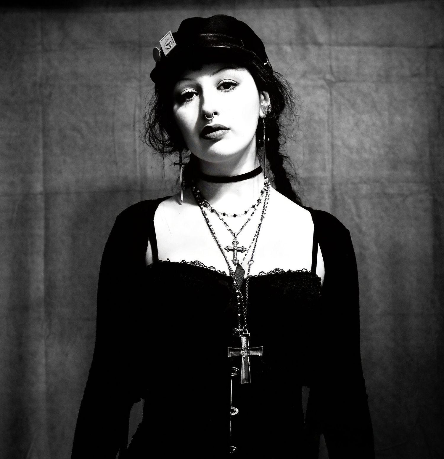 Black and white editorial portrait of a woman in a Victorian-style dress with layered necklaces, leather cap, and moody studio lighting.